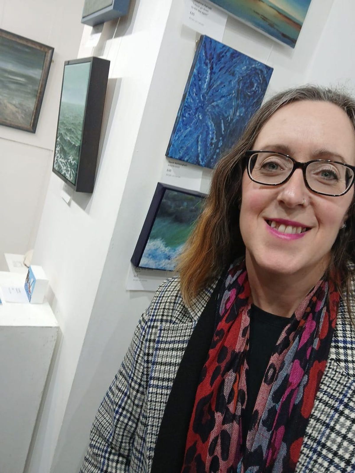 Fiona smiling beside her framed paintings hung on a gallery wall