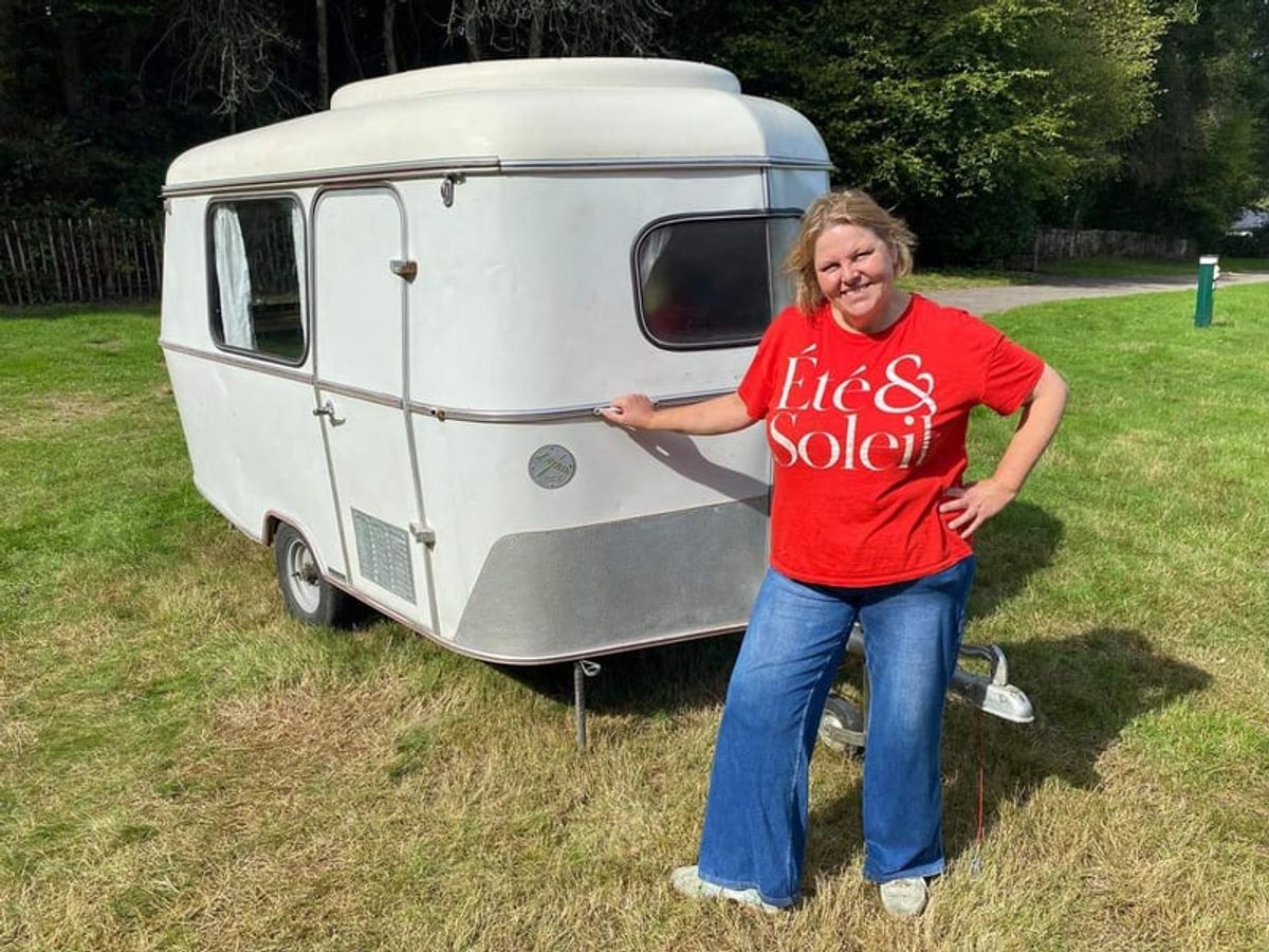 Joanne standing beside a small vintage caravan on grass, hand on the door
