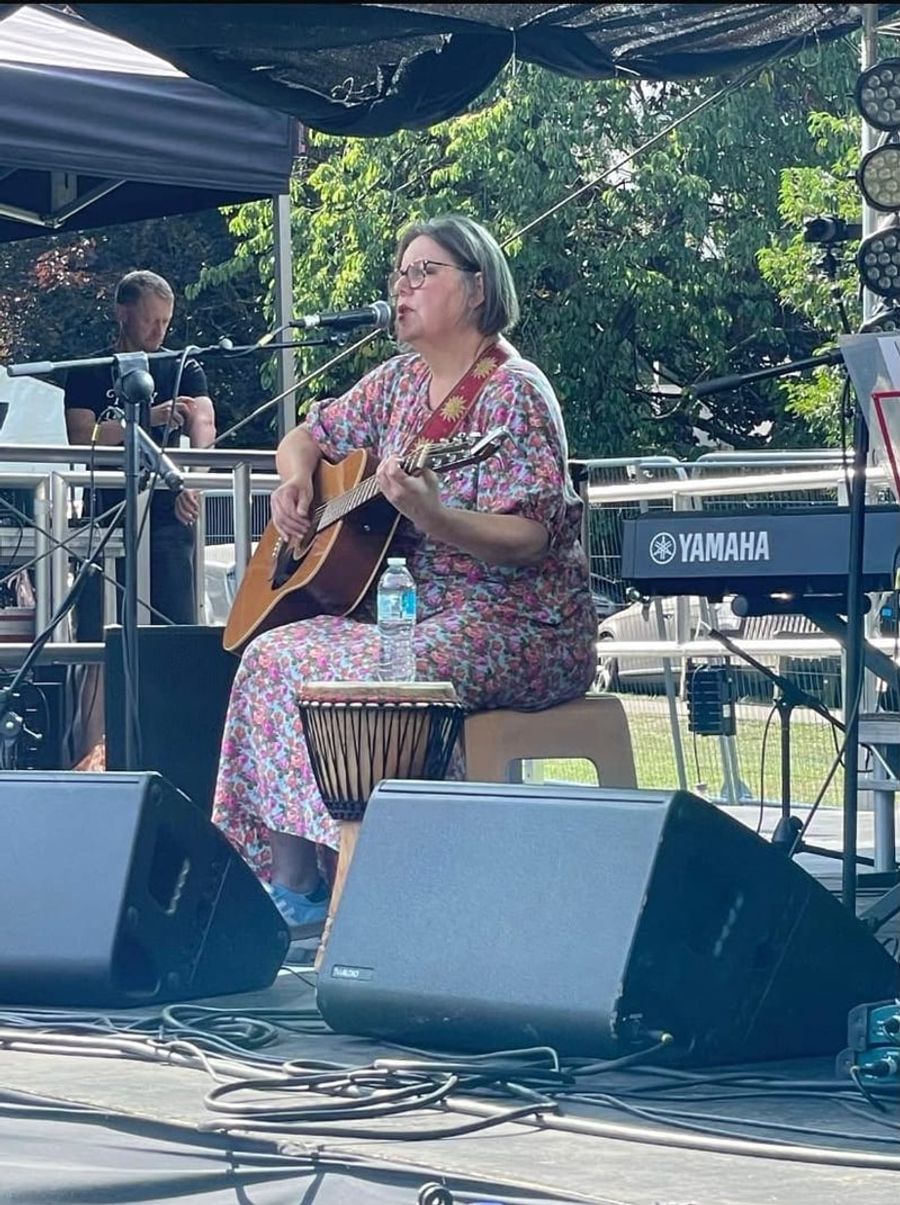 Joanne on an outdoor stage playing an acoustic guitar and singing into a microphone