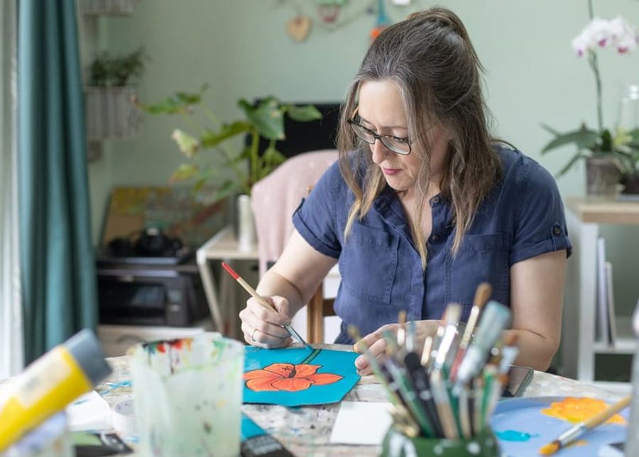 Fiona painting at a table in her studio, brush in hand