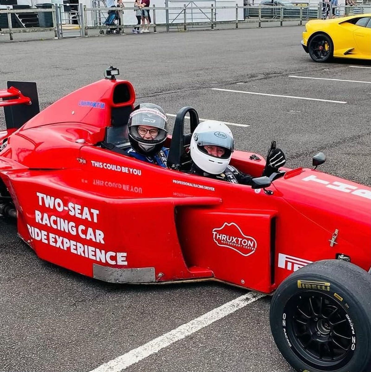 Two people in racing helmets riding together in an open-top racing car