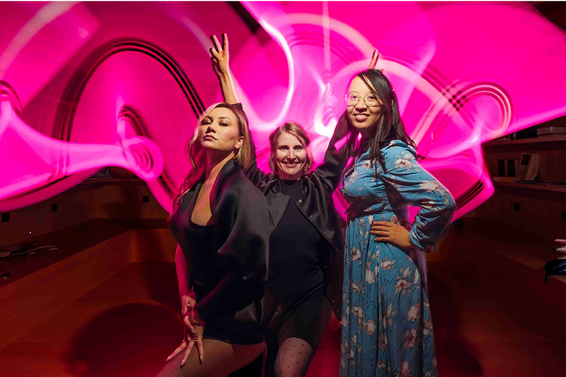 Three guests at the Hearts & Science launch event in front of a pink light installation