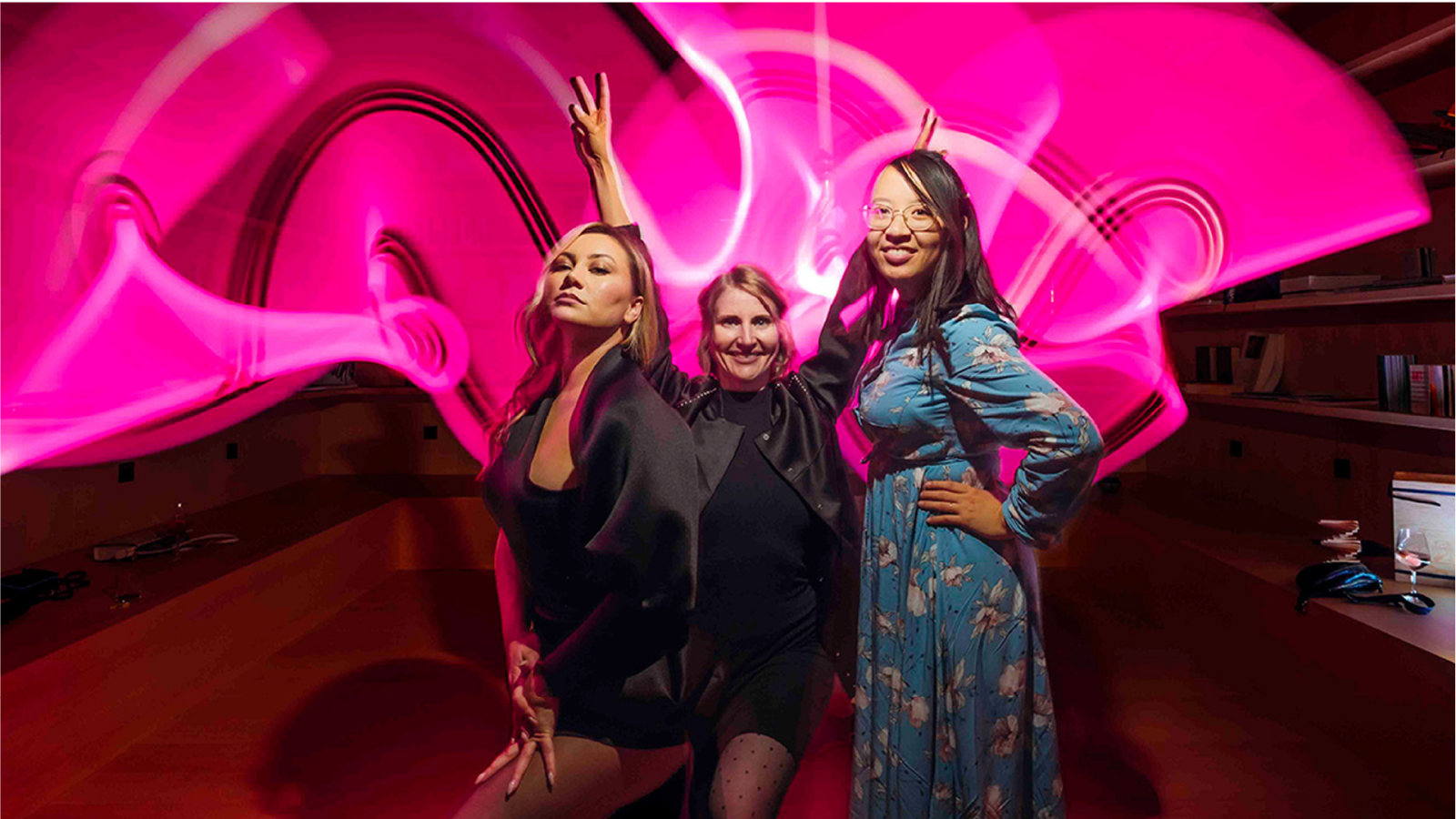 Three guests at the Hearts & Science launch event in front of a pink light installation