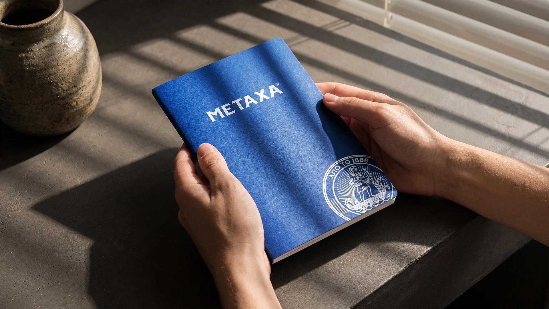 Modrý firemní sešit Metaxa v rukou na betonovém parapetu