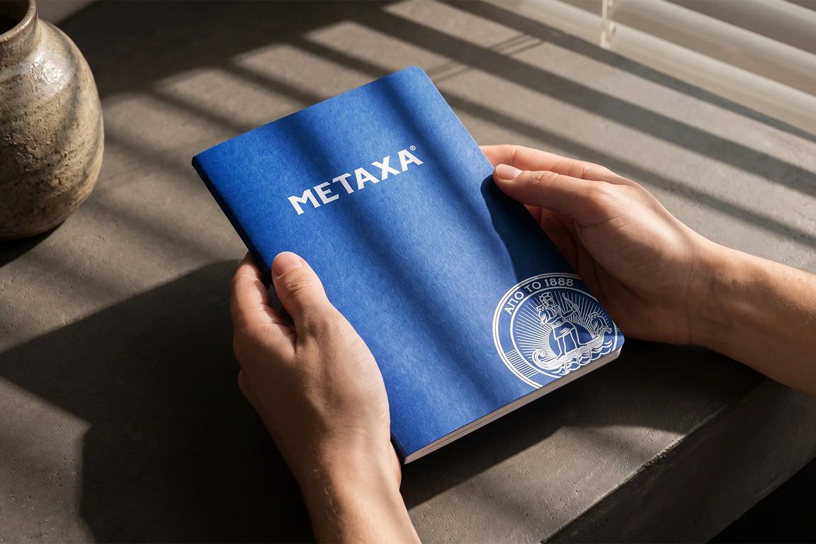 Modrý firemní sešit Metaxa v rukou na betonovém parapetu