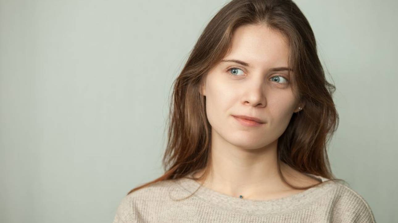 Vrouw met lang bruin haar kijkt peinzend opzij tegen een lichtgrijze achtergrond
