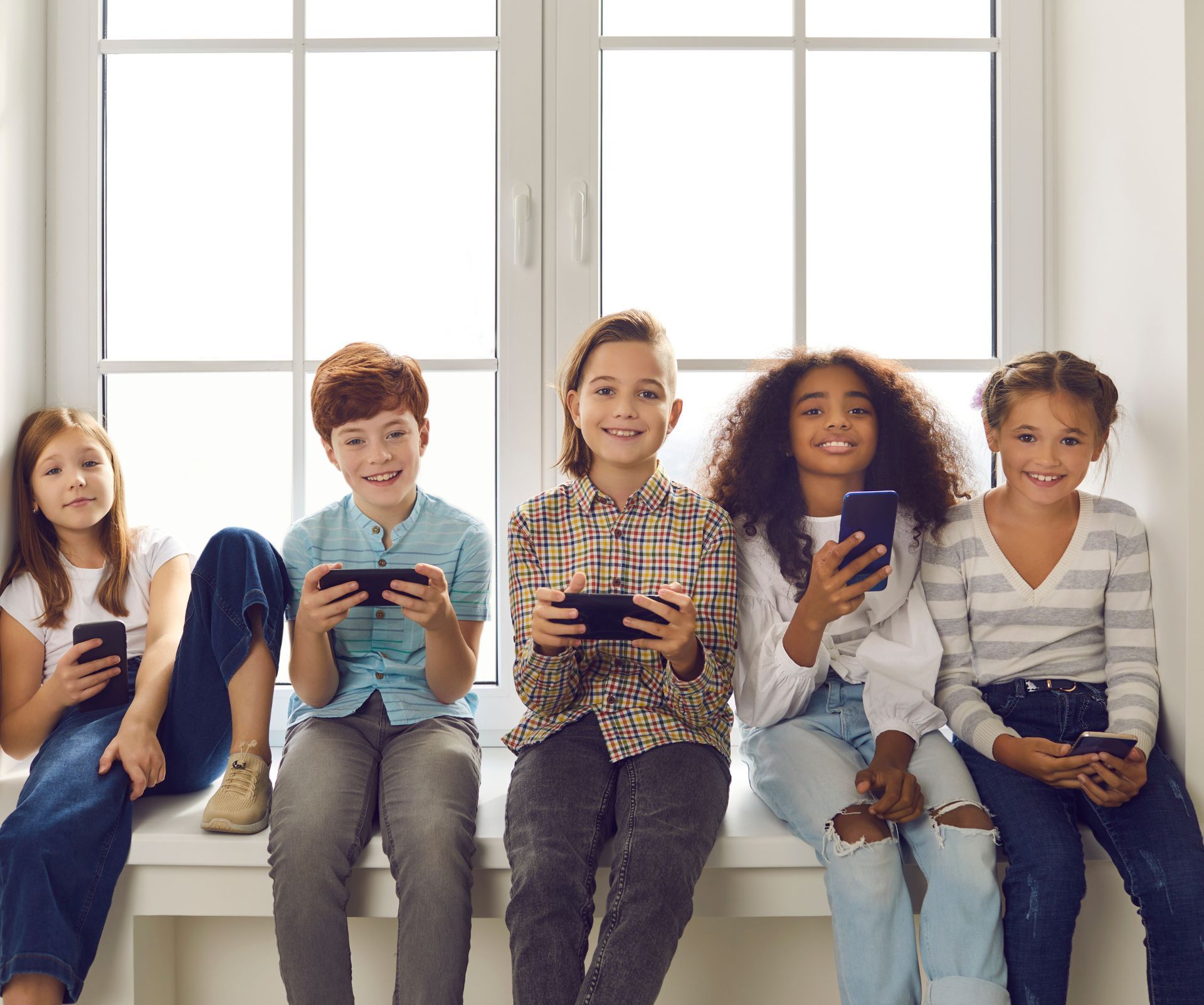 Vijf kinderen zitten naast elkaar op een vensterbank, elk met een smartphone in de hand