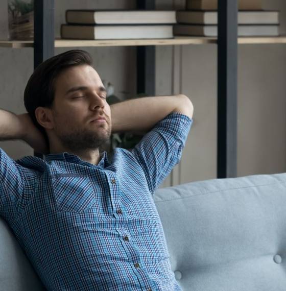 Persoon leunt met de handen achter het hoofd en gesloten ogen ontspannen achterover op een bank