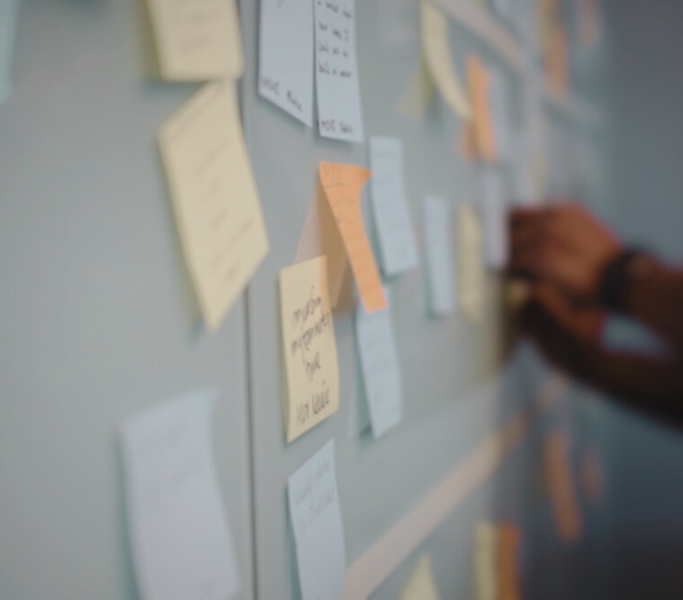 Wand vol beschreven post-its tijdens een workshop, een hand plakt er een briefje bij