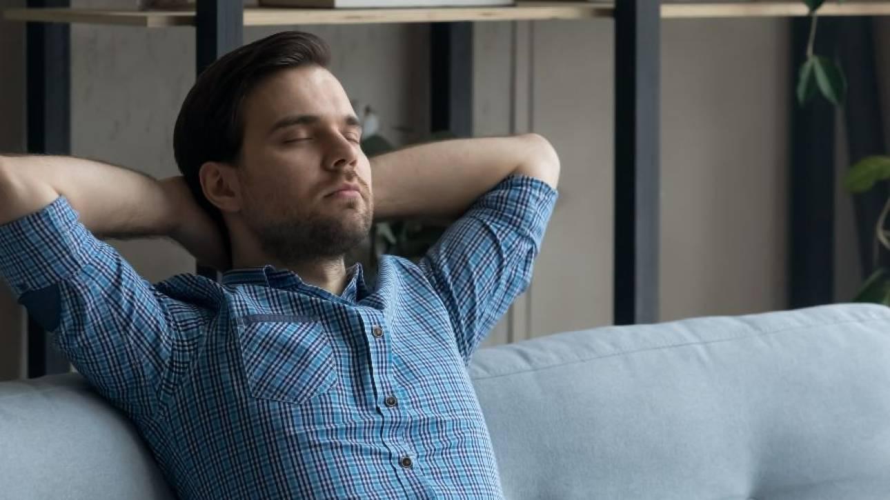 Man leunt ontspannen achterover op een bank, handen achter het hoofd en de ogen gesloten