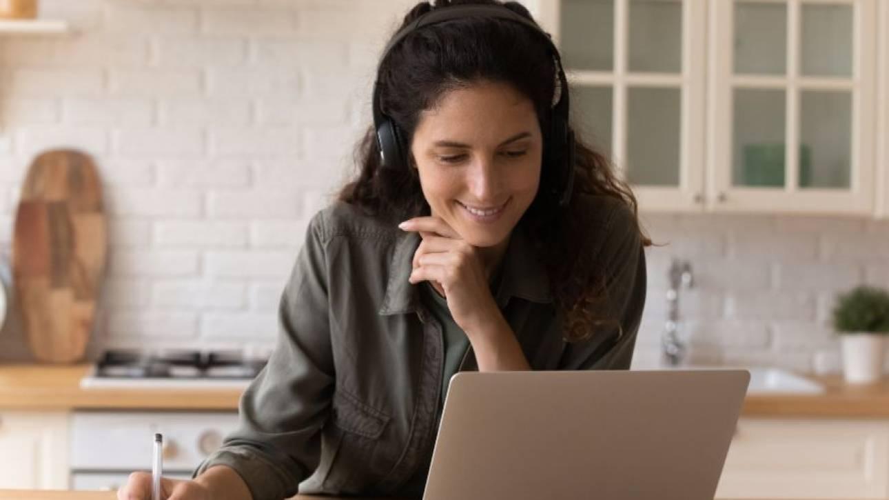 Persoon met koptelefoon volgt lachend een online sessie achter een laptop en maakt aantekeningen