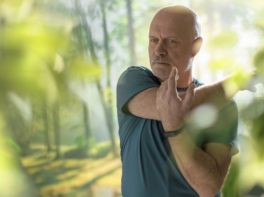 Persoon in sportshirt rekt de schouder uit in een groene omgeving met bomen