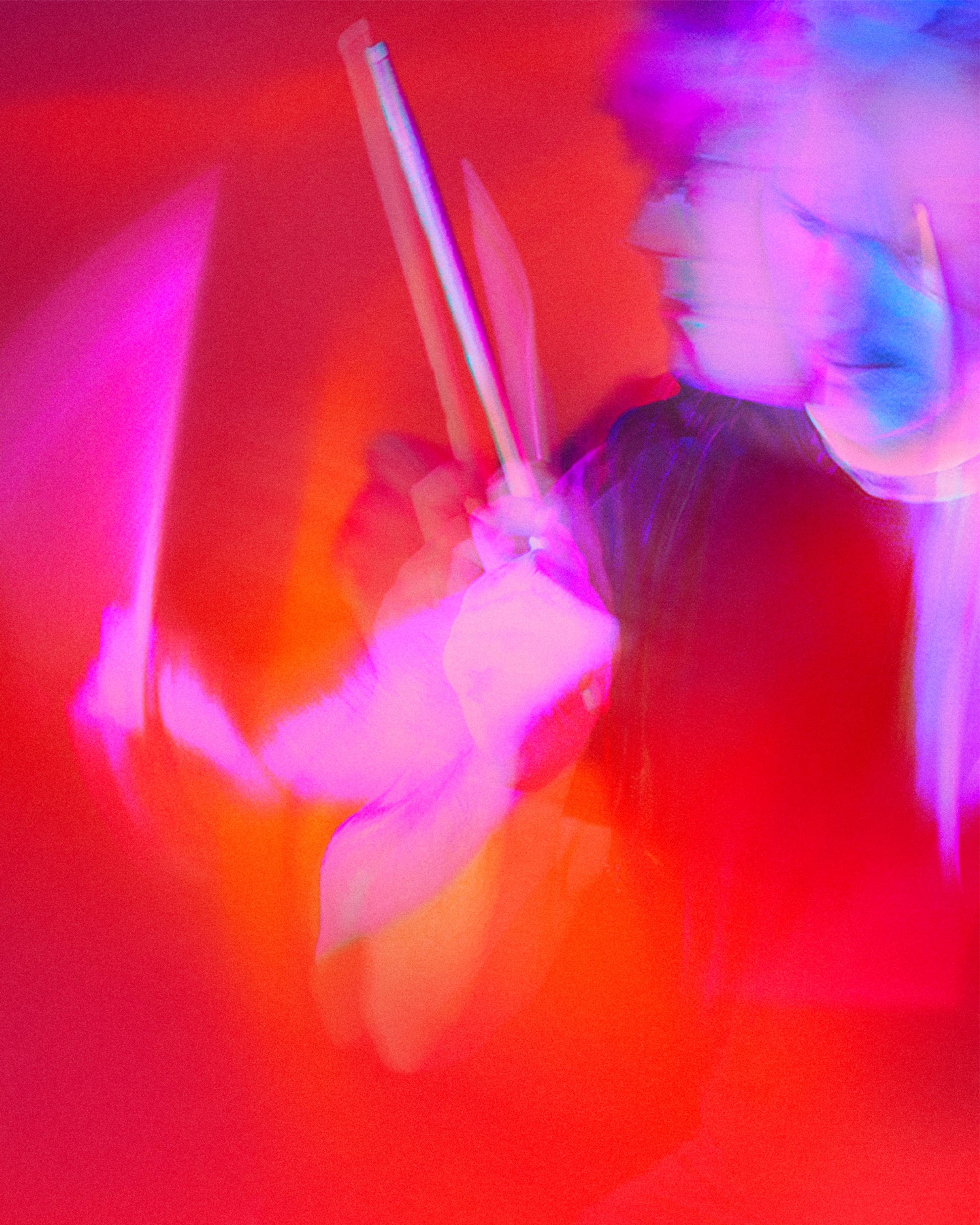A drummer mid-beat in red and pink light, sticks blurred with movement