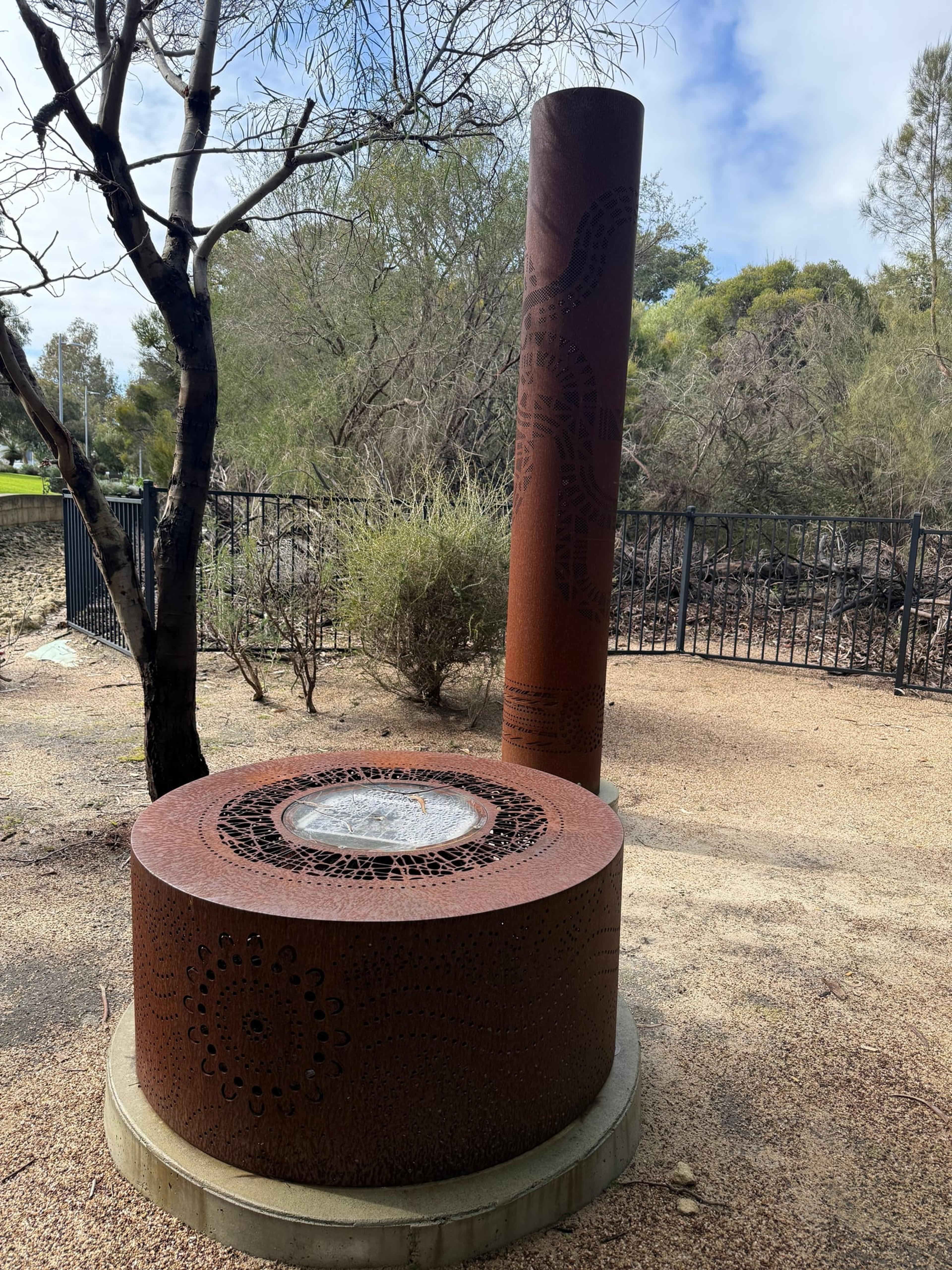 The fire pit in front of a rusted totem, five years on