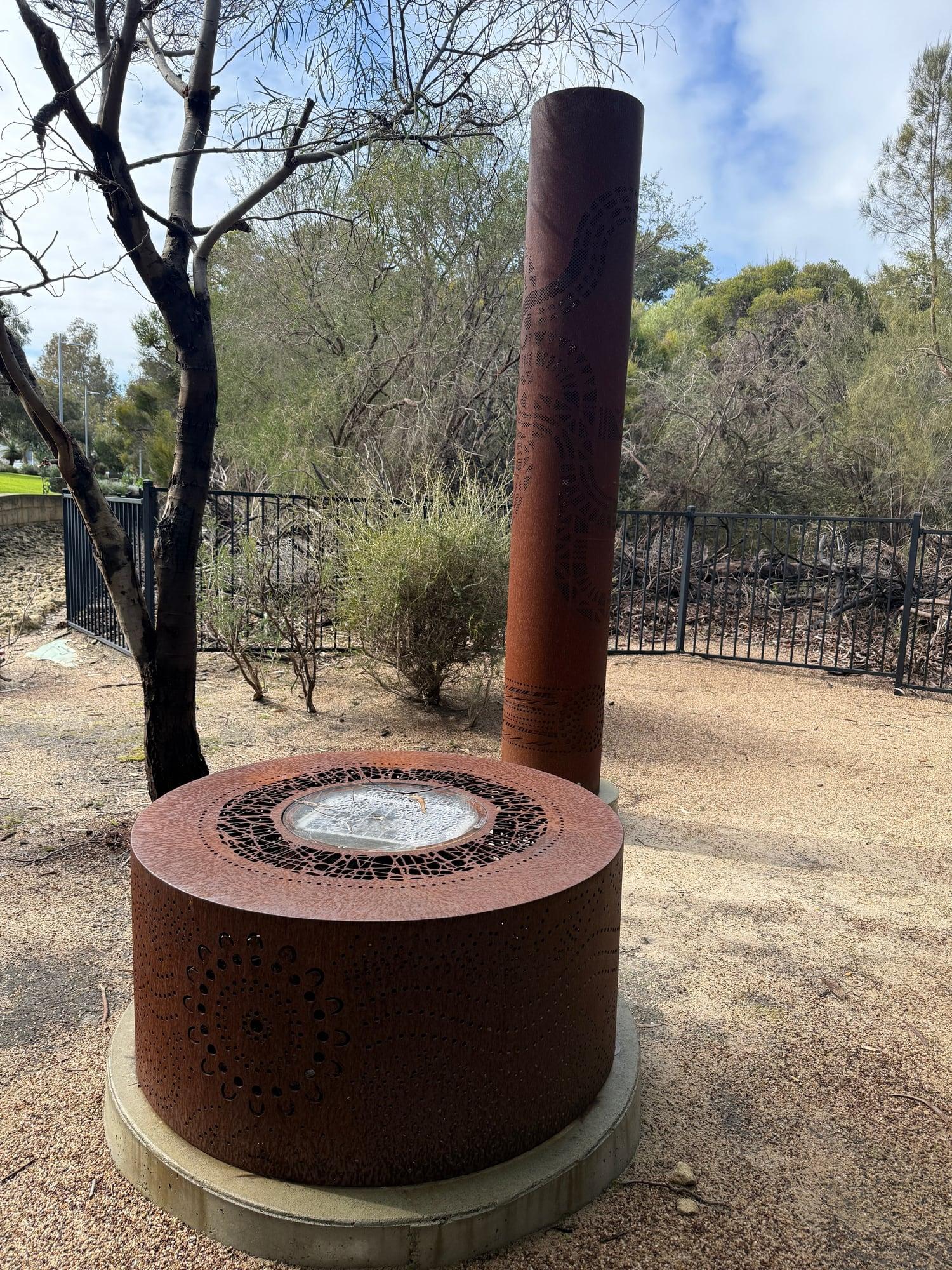 The fire pit in front of a rusted totem, five years on