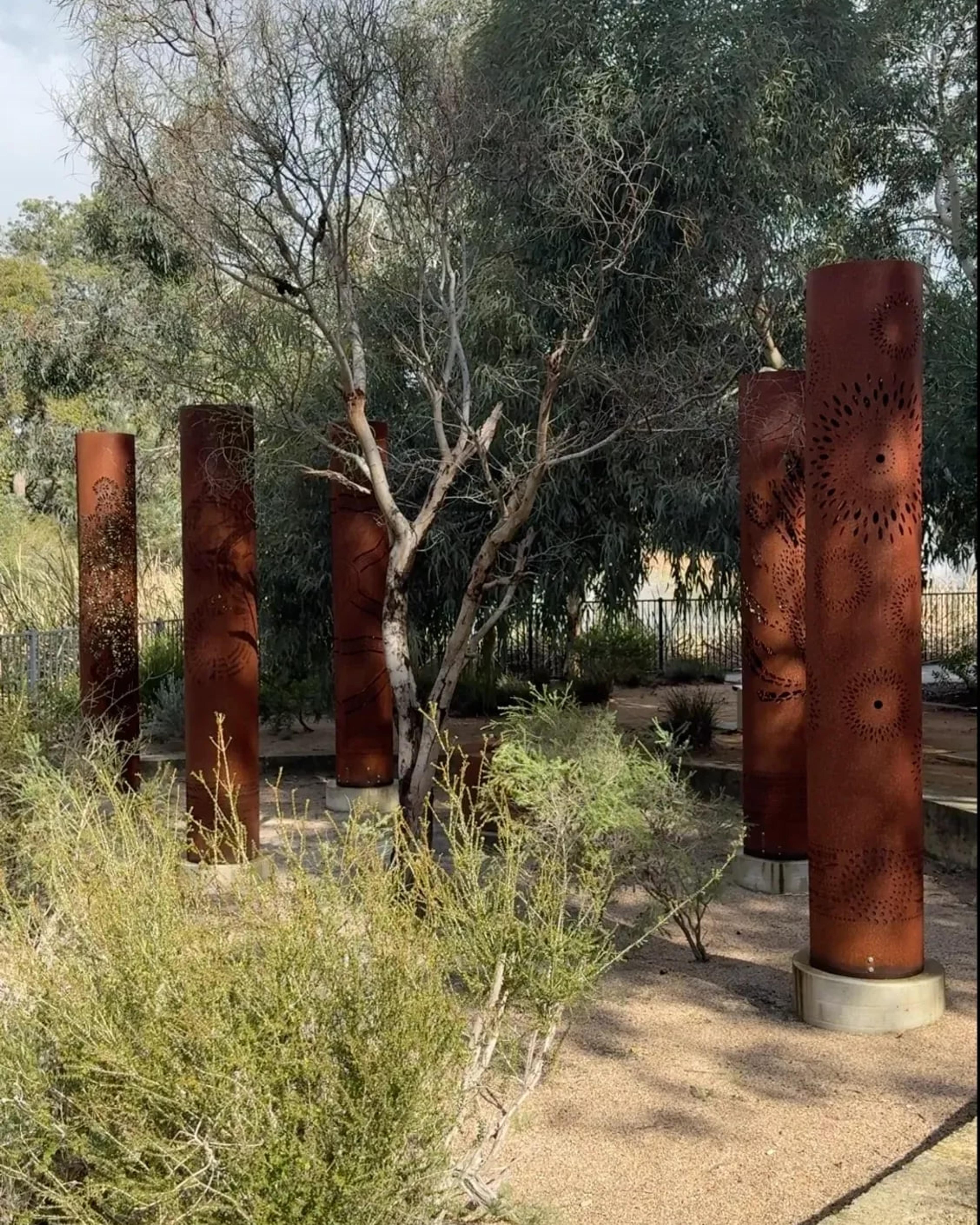 Rusted corten steel totems among native plants and a bare tree in the hospital gardens
