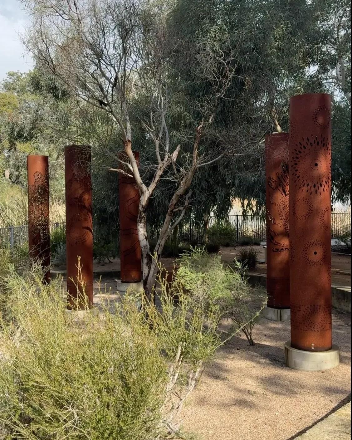 Rusted corten steel totems among native plants and a bare tree in the hospital gardens
