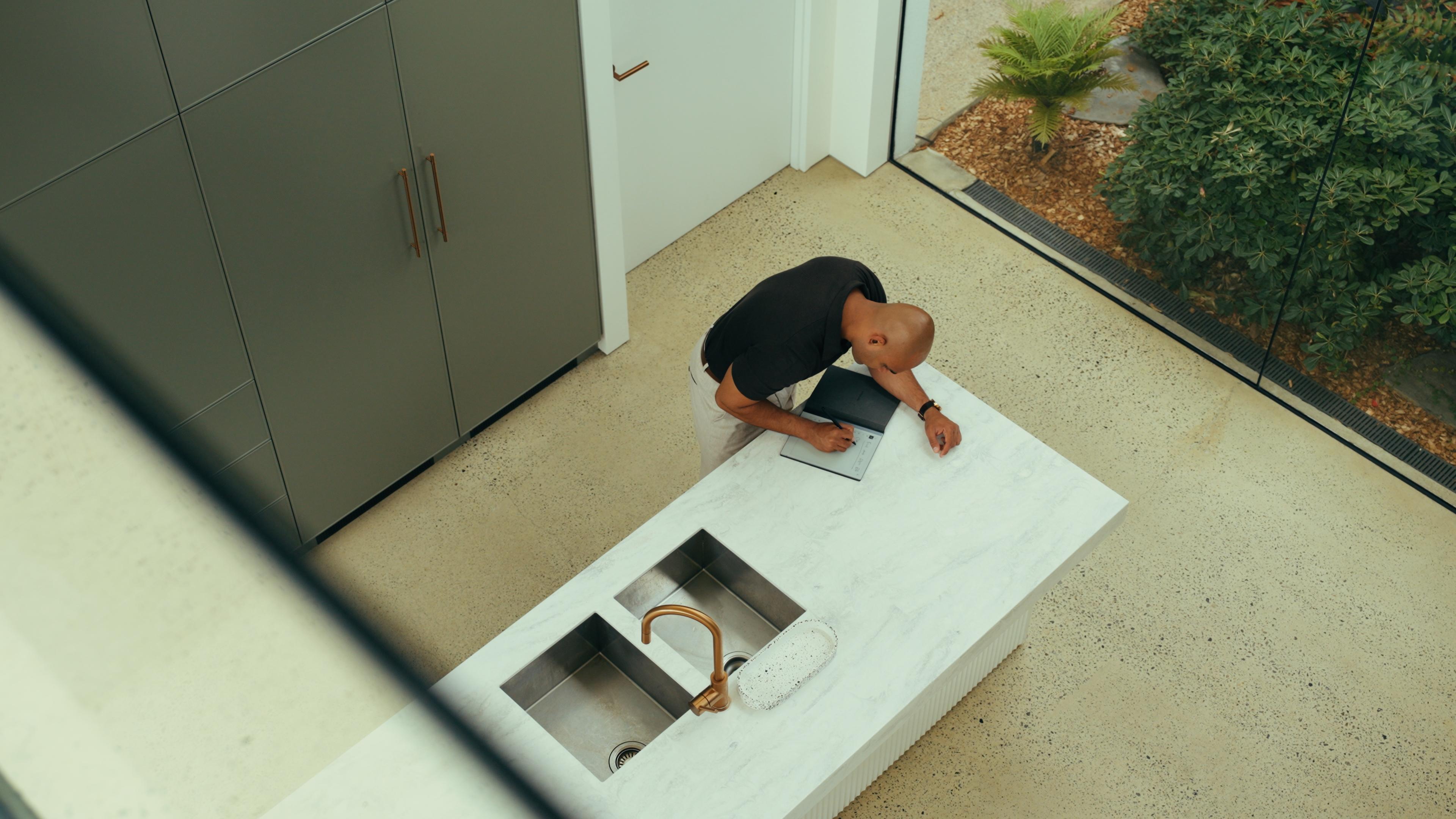 Find & Sign’s Niki inspecting a home, seen from above making notes at the kitchen bench