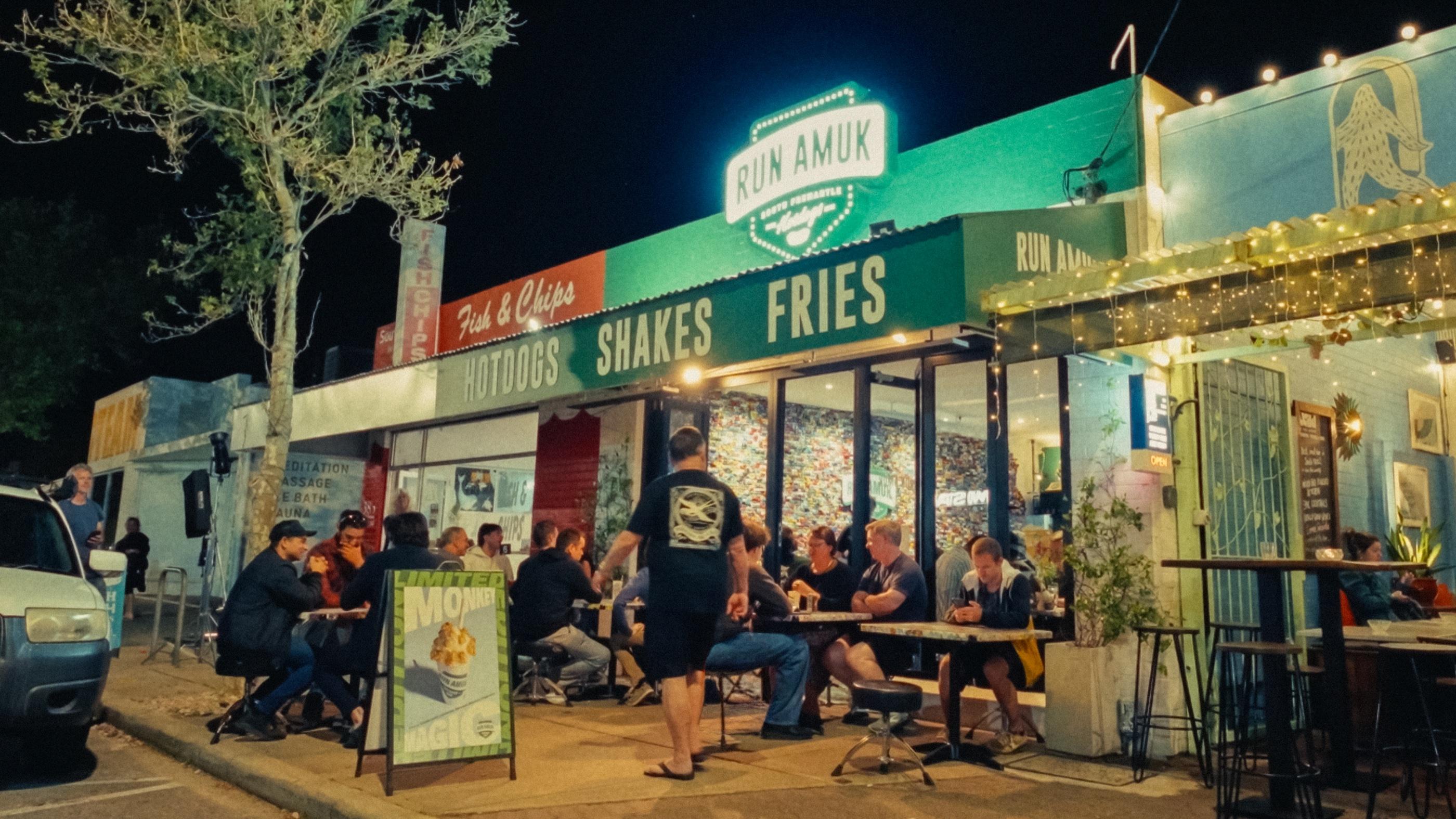 Run Amuk’s lit shopfront at night with diners on the footpath