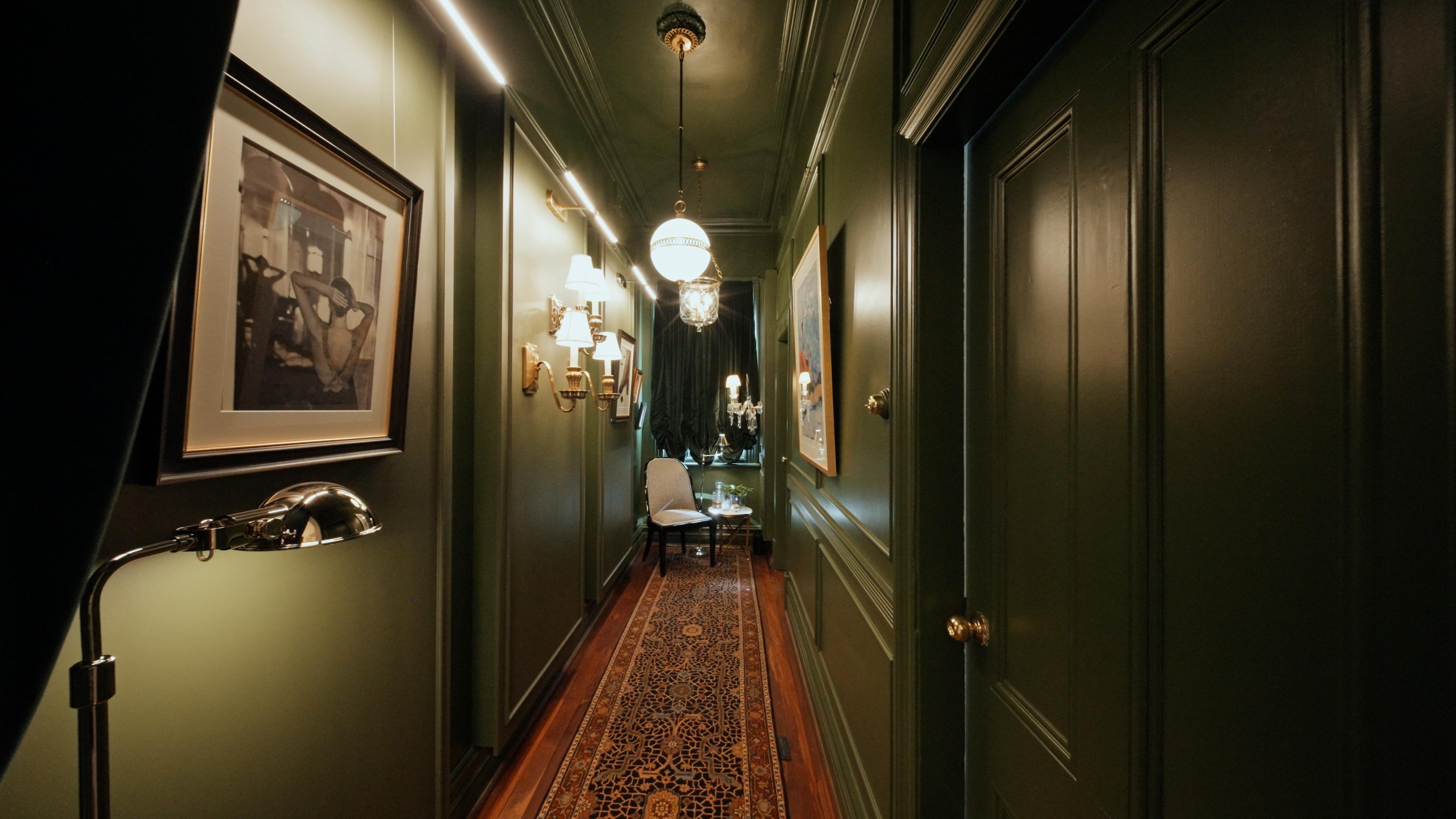 A green panelled hallway with a patterned runner and brass wall lights