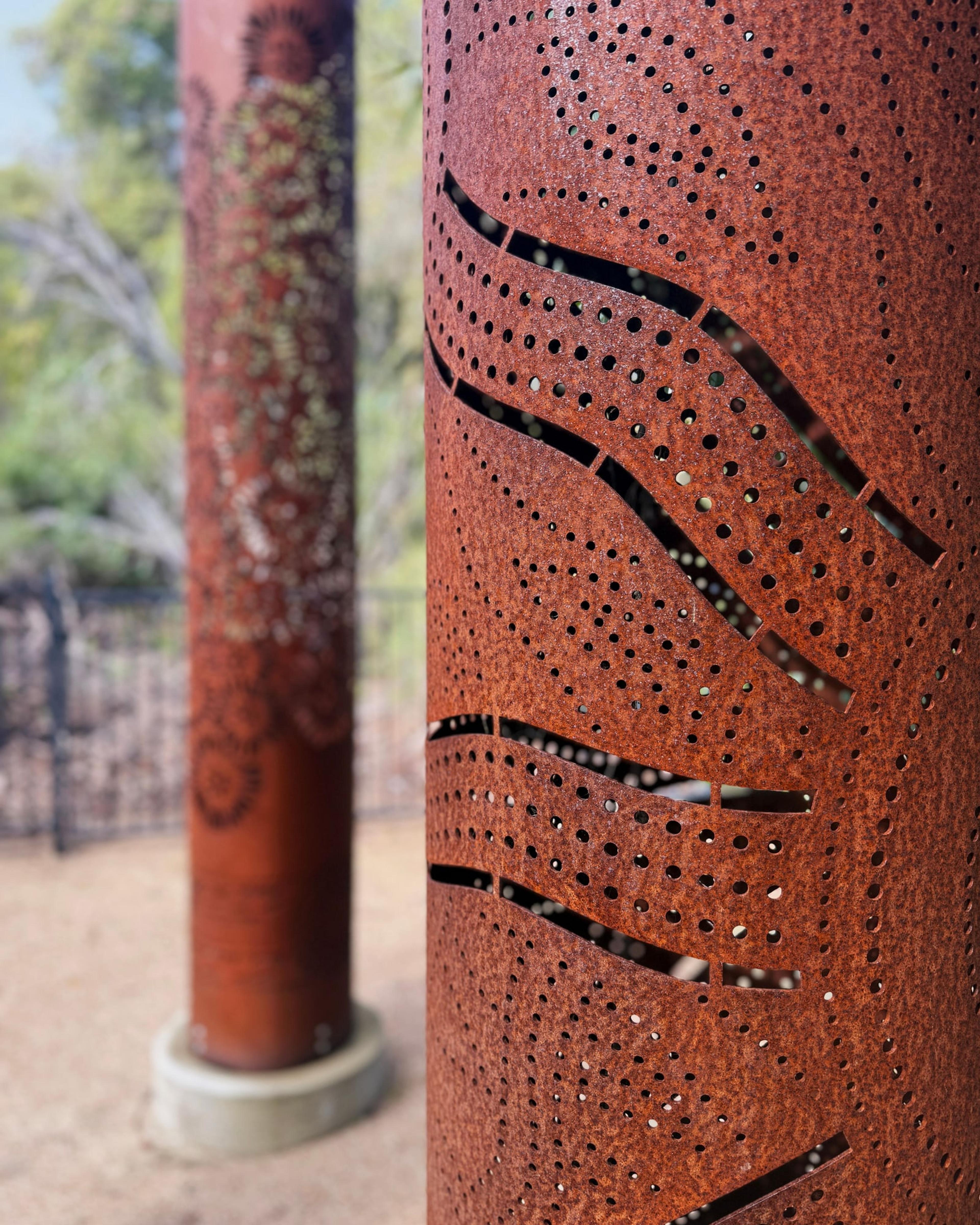 Close view of wavy cut lines and dots in a rusted totem, with another totem behind
