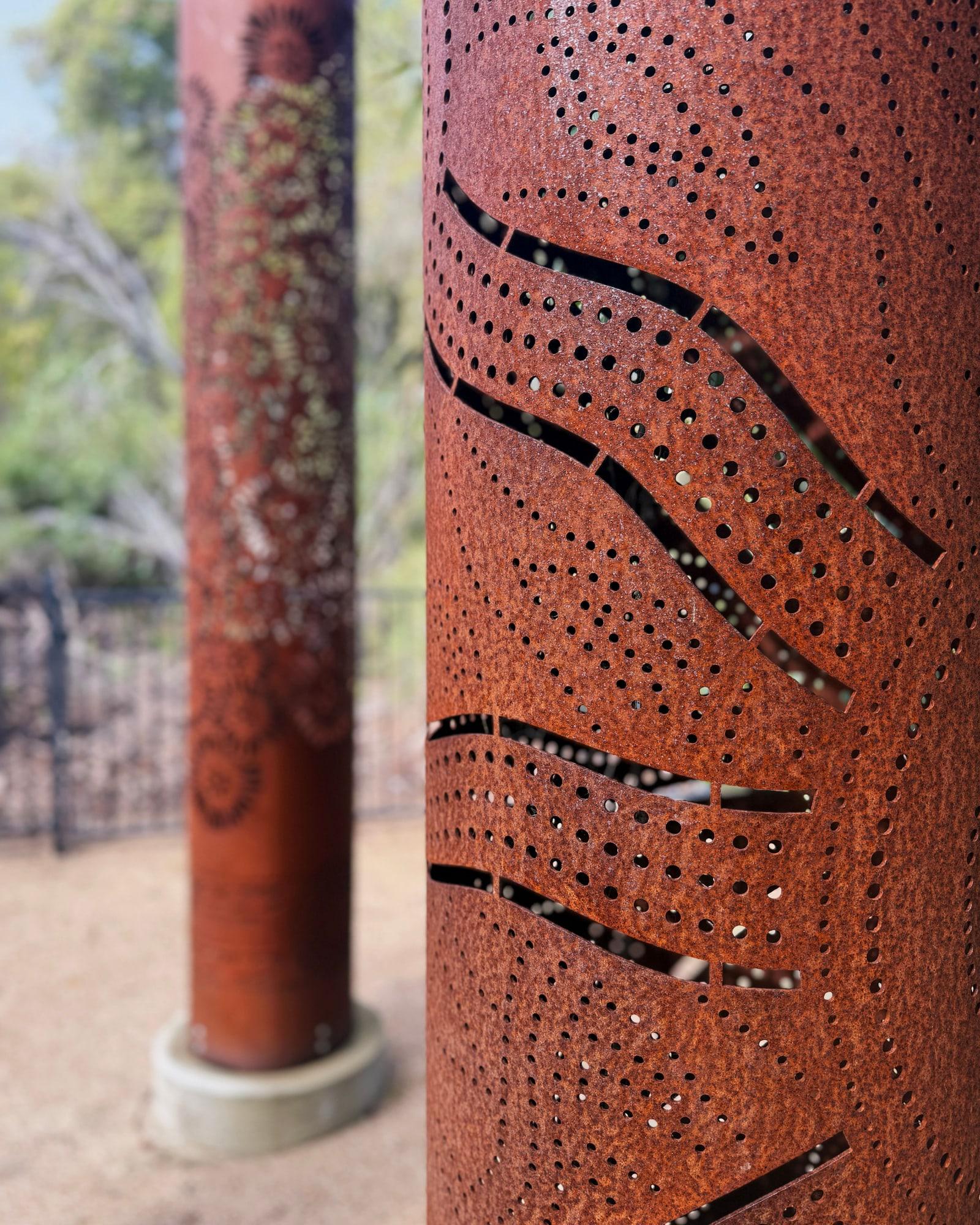Close view of wavy cut lines and dots in a rusted totem, with another totem behind