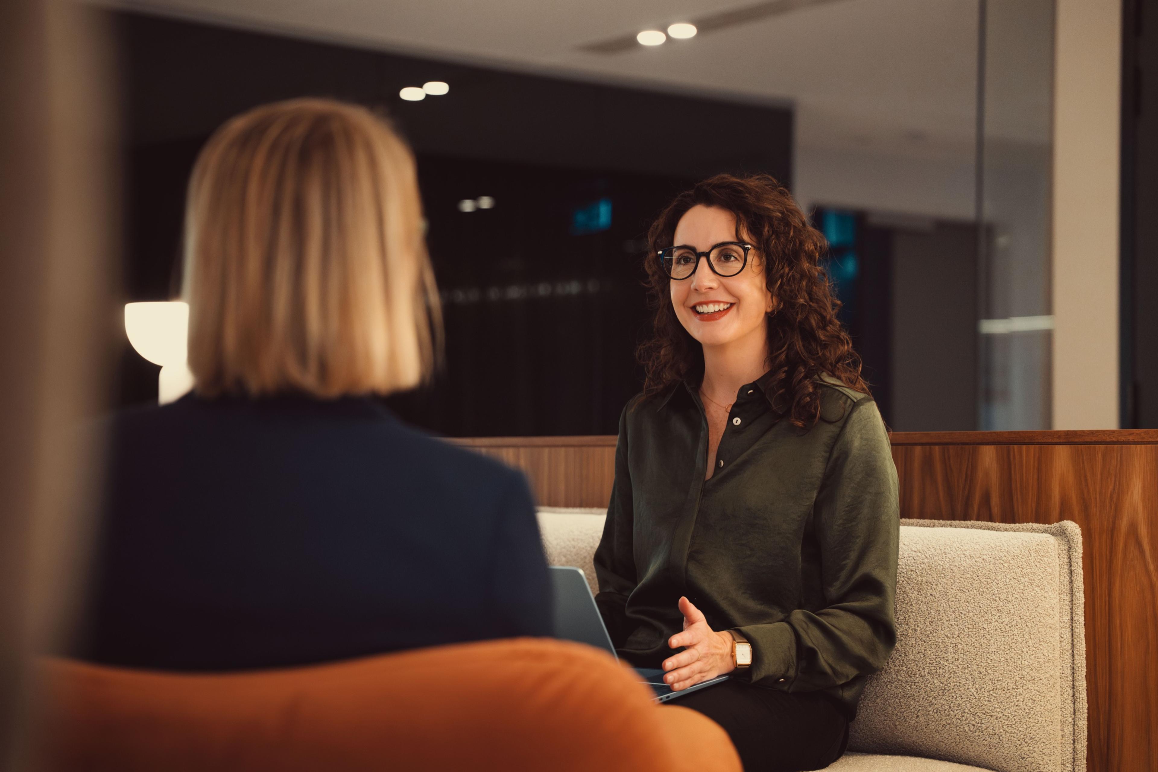 An AKT Advisory partner smiling as she talks with a client in an office lounge