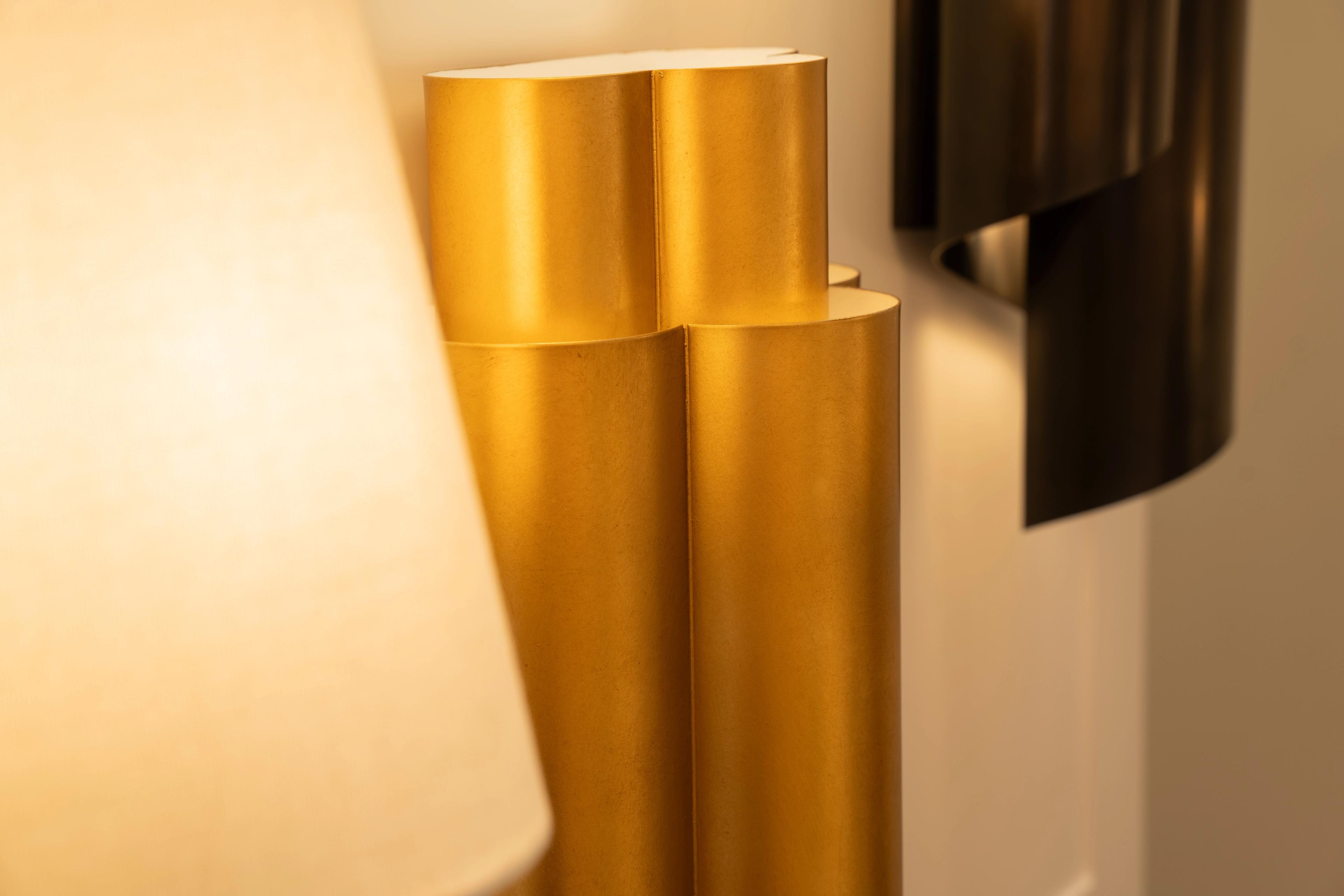 A brushed brass sculptural lamp beside a dark metal sconce