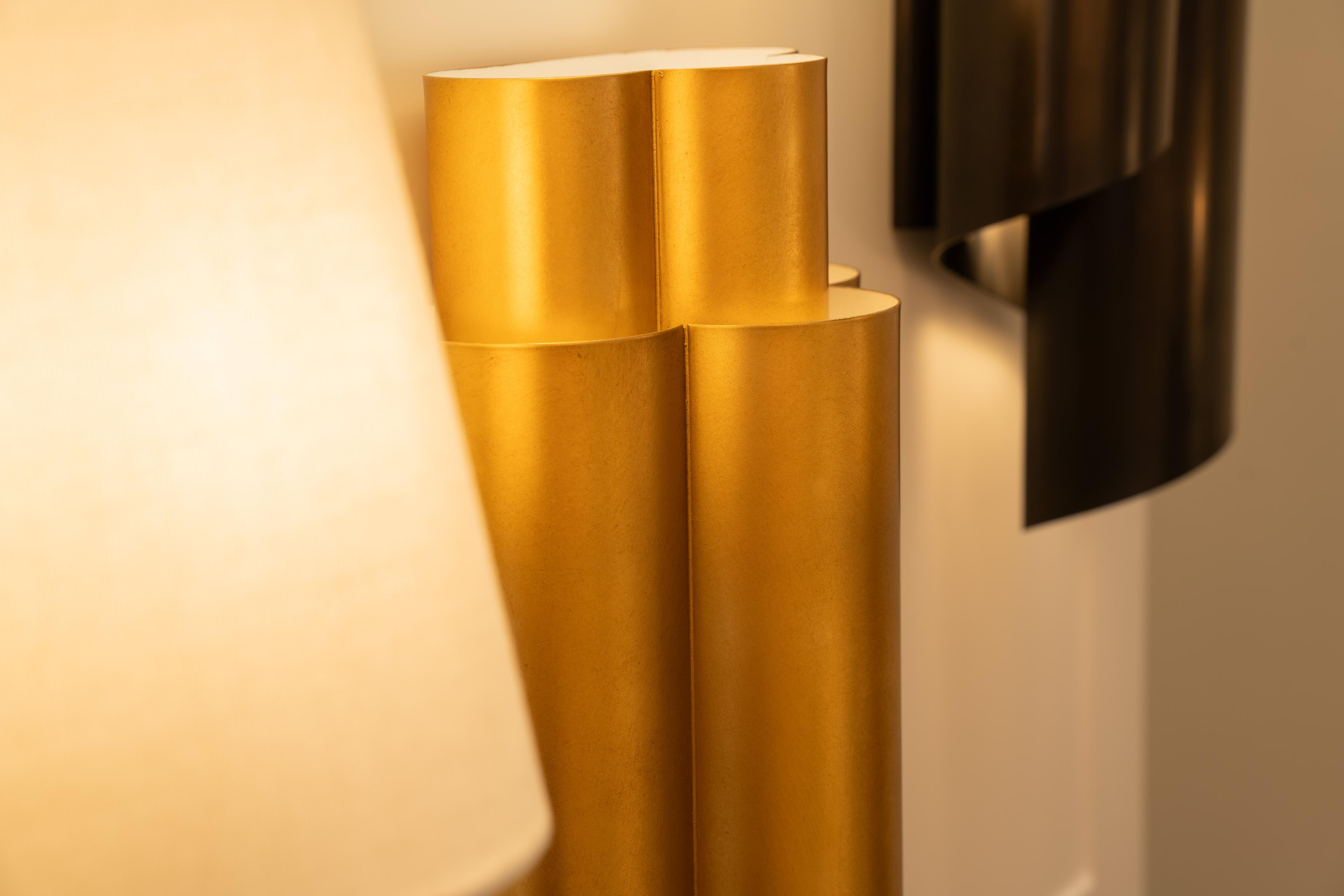 A brushed brass sculptural lamp beside a dark metal sconce