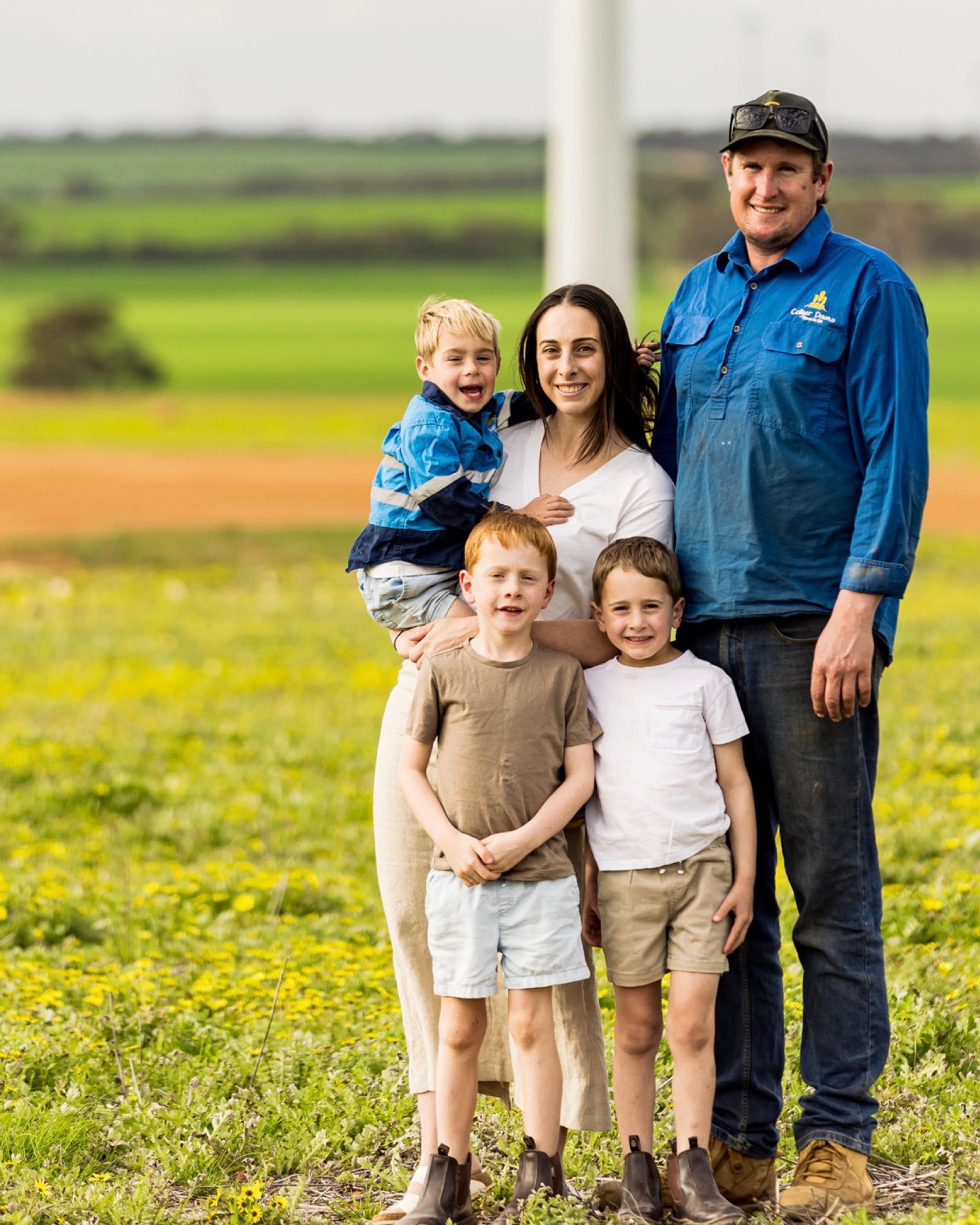 A farming family of five standing in a wildflower paddock beneath a turbine at Collgar Wind Farm