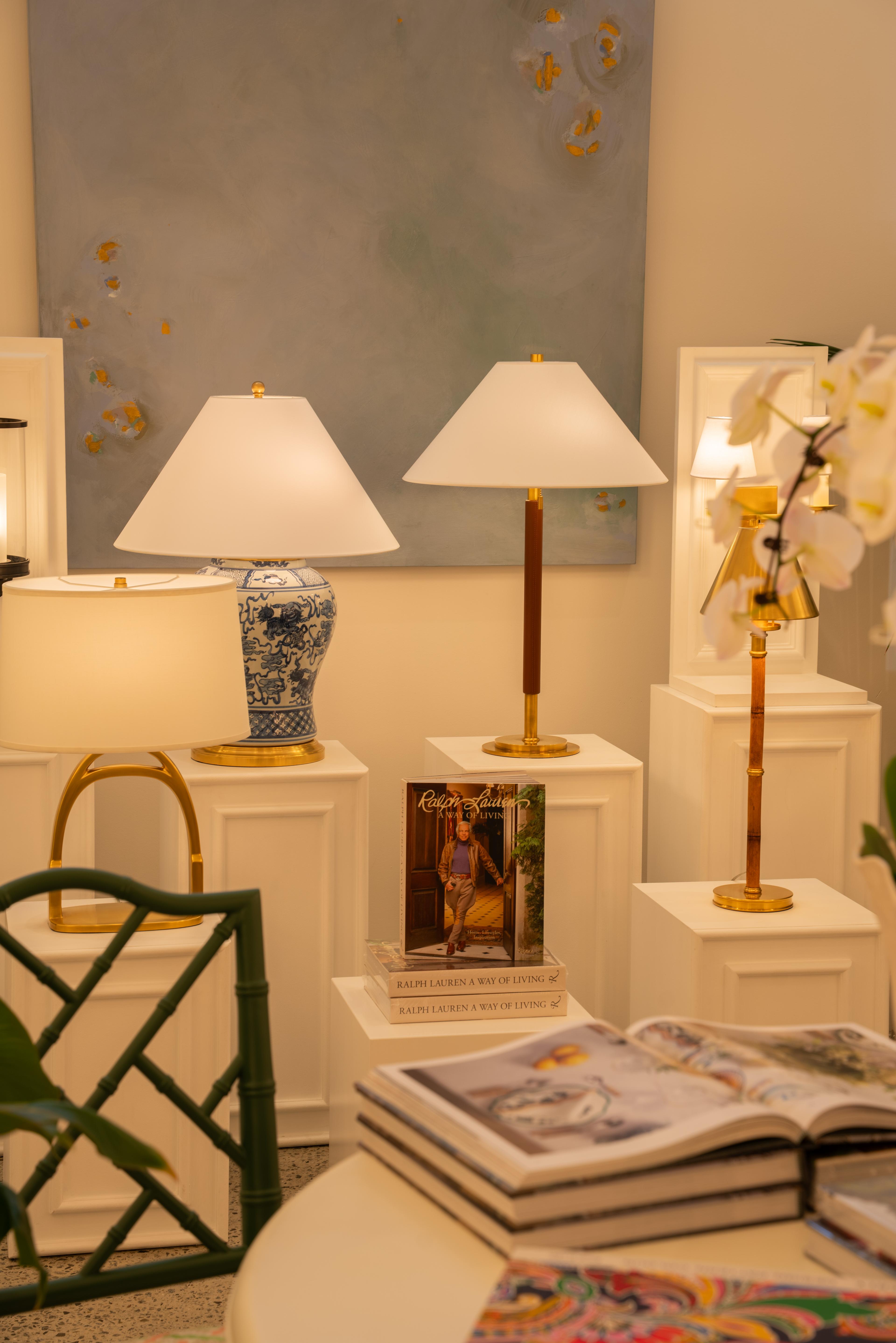 Table lamps on white plinths beside a stack of books and orchids