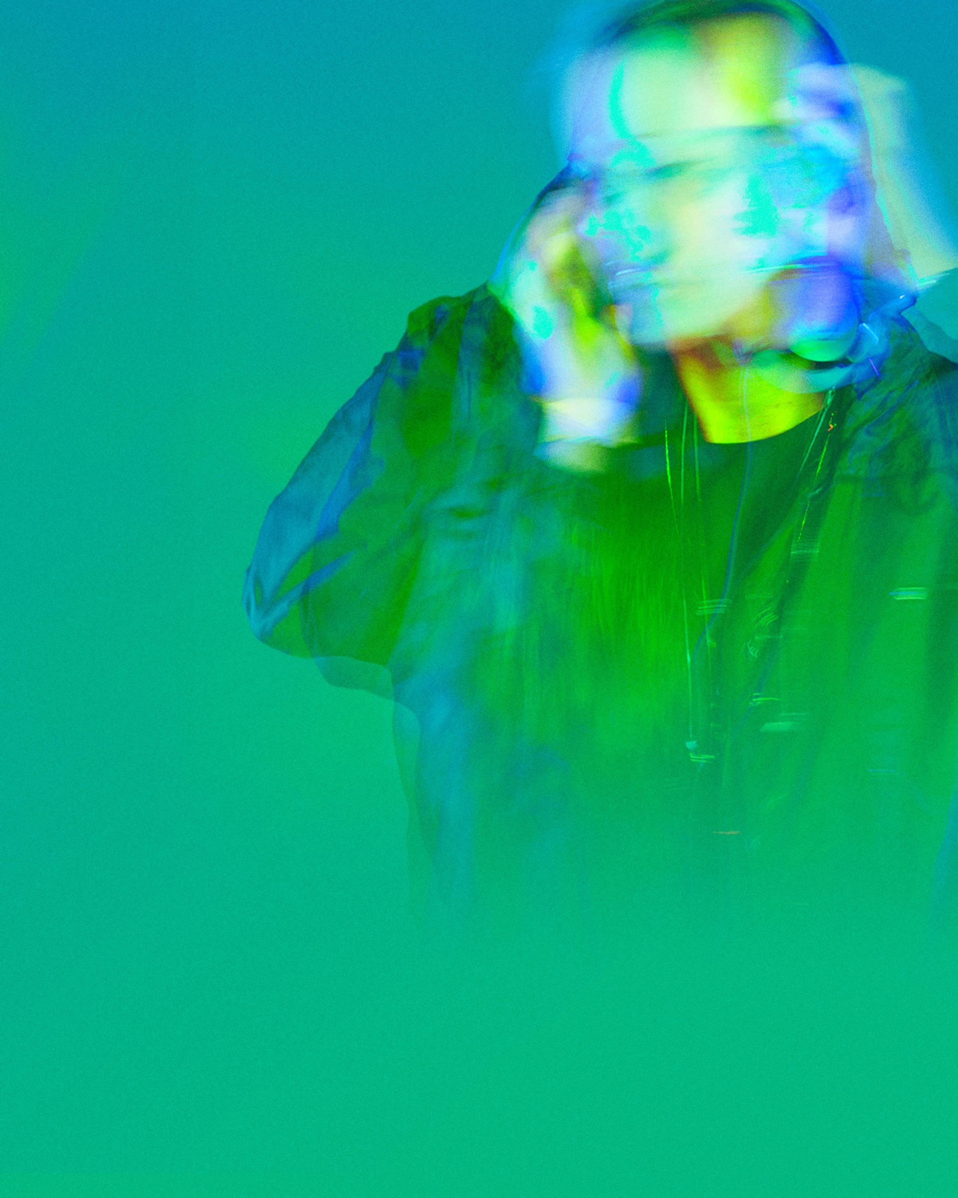 A DJ with headphones on, washed in green and aqua light