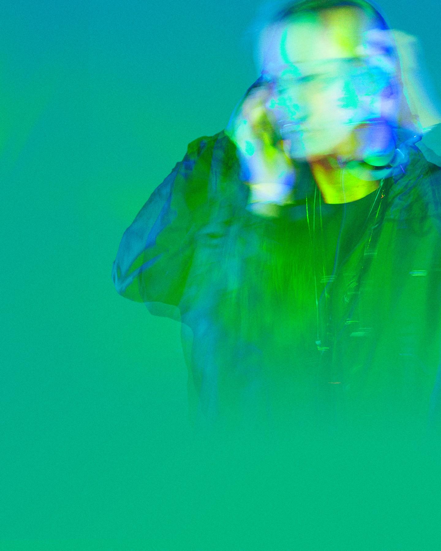 A DJ with headphones on, washed in green and aqua light