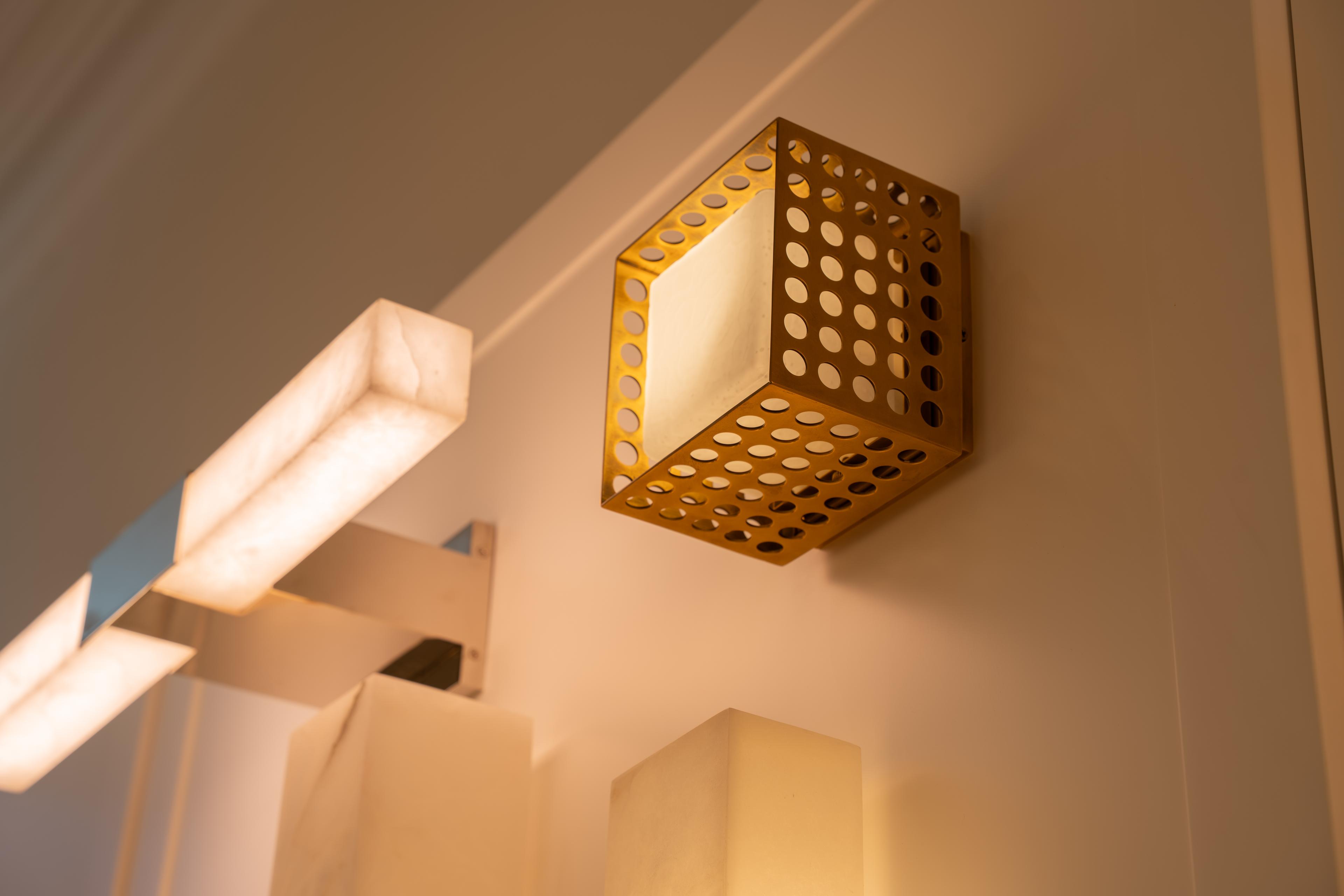 A perforated brass cube wall light beside alabaster bar lights