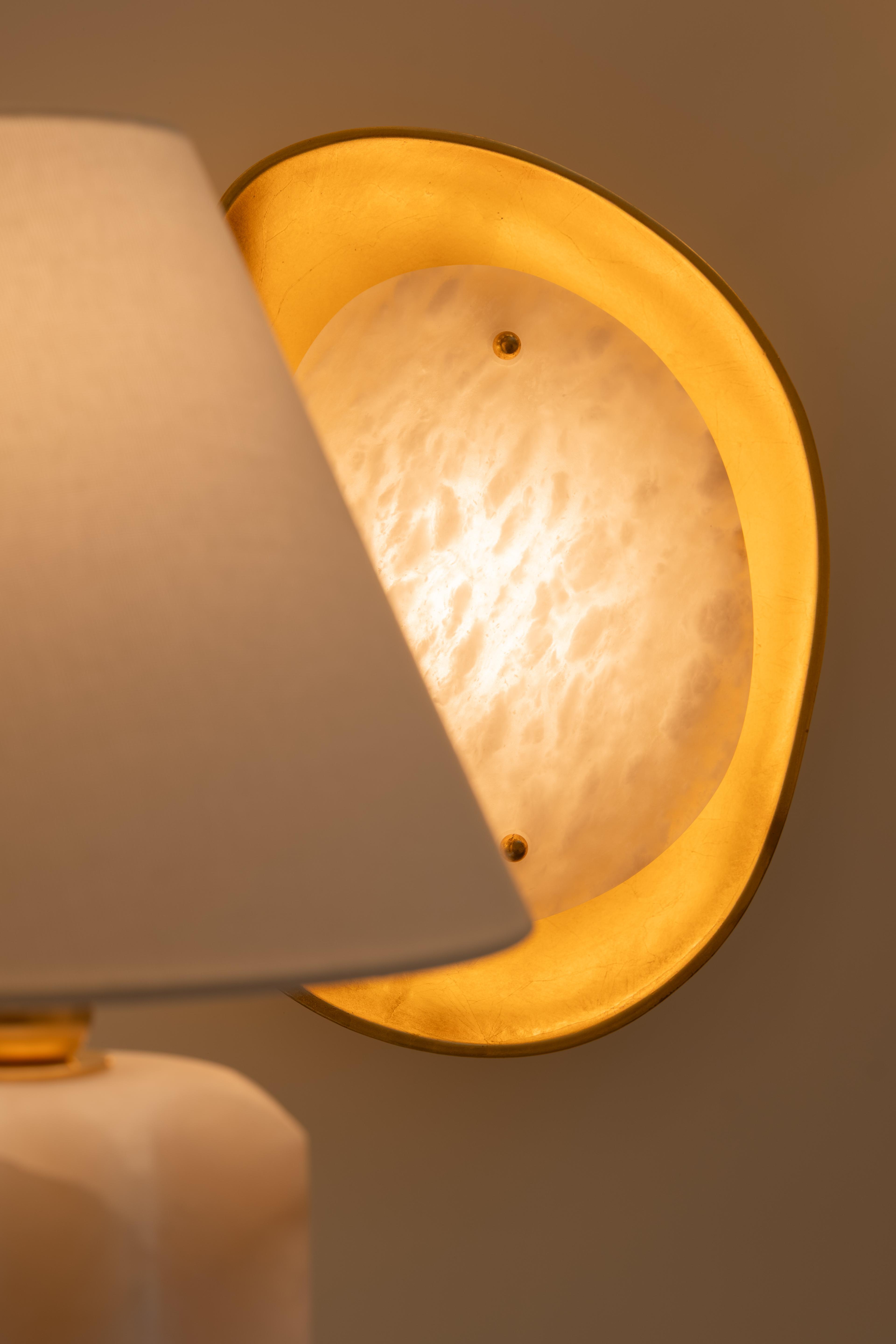 An alabaster and brass wall light behind a pleated lamp shade