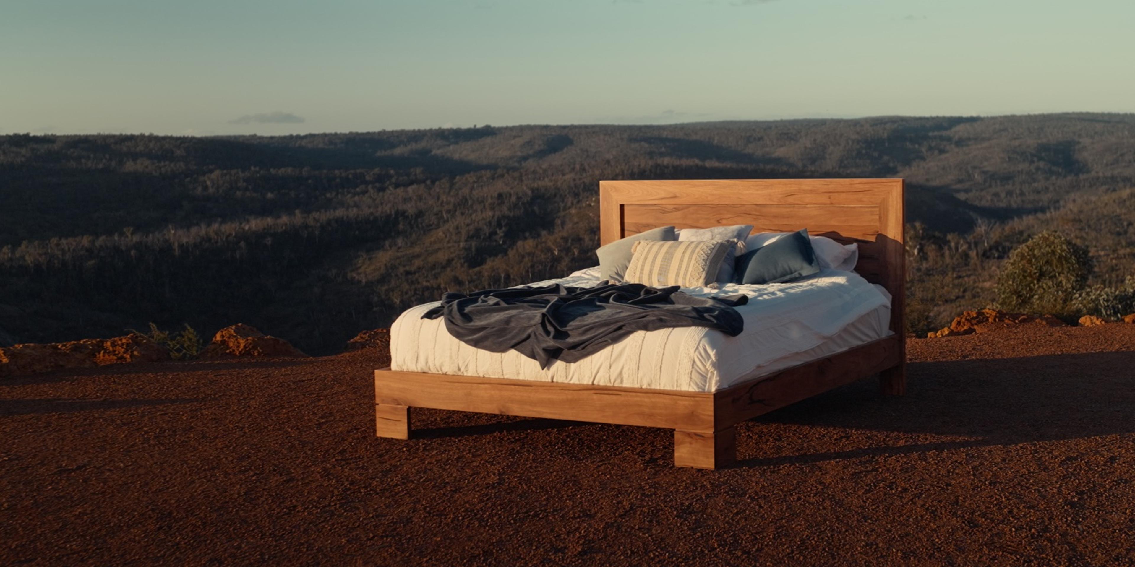 Roleystone king bed made up on red earth above a valley at dusk