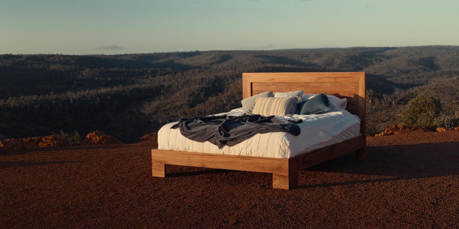 Roleystone king bed made up on red earth above a valley at dusk