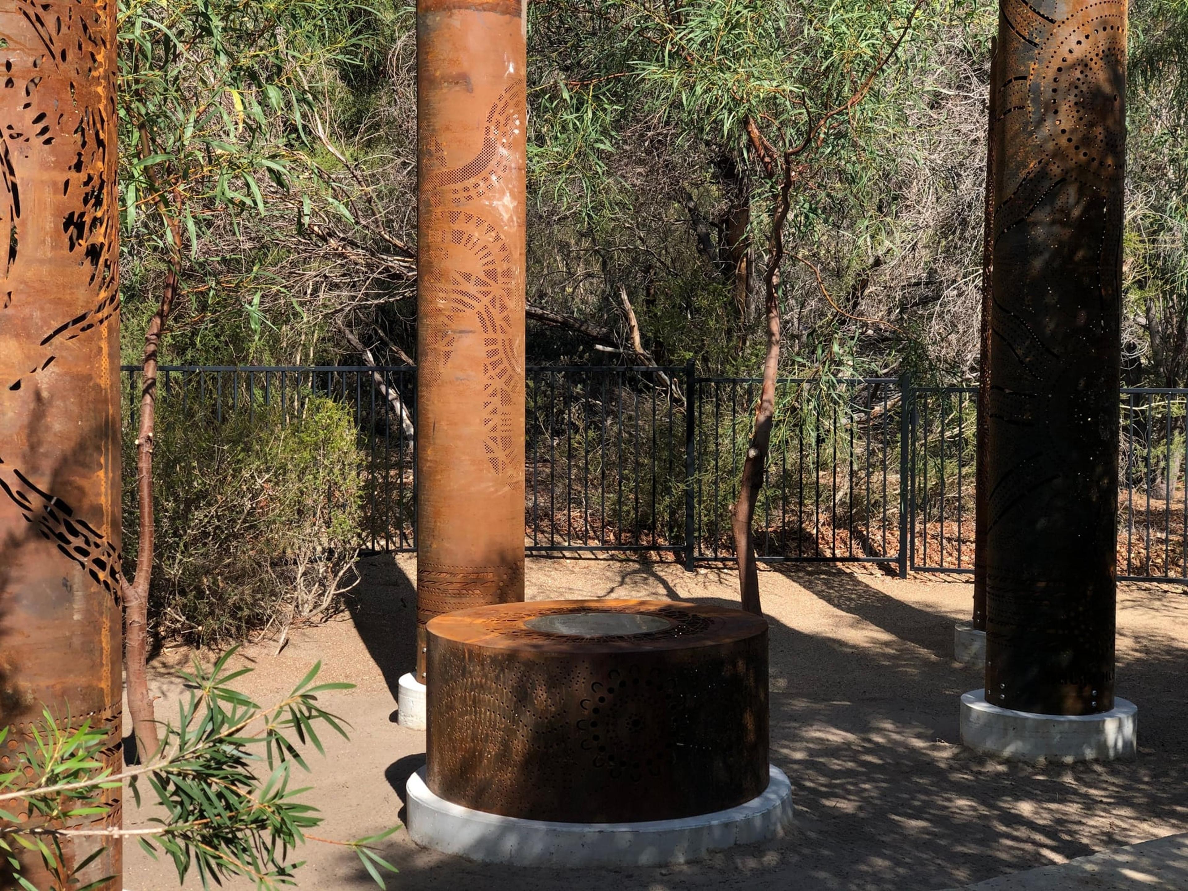 The fire pit between three totems in dappled light