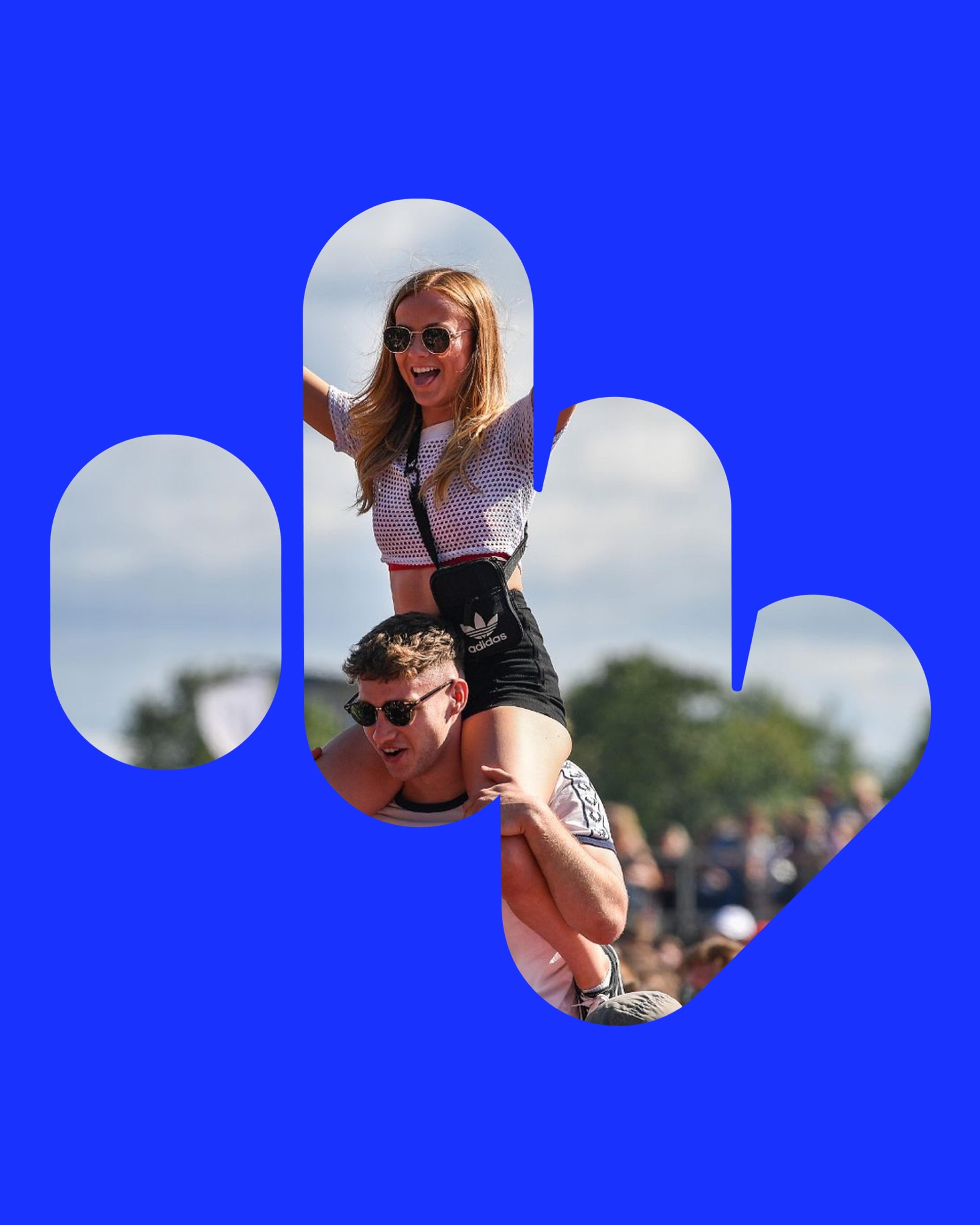 A fan on a friend’s shoulders at a festival, framed by the Massive symbol on blue