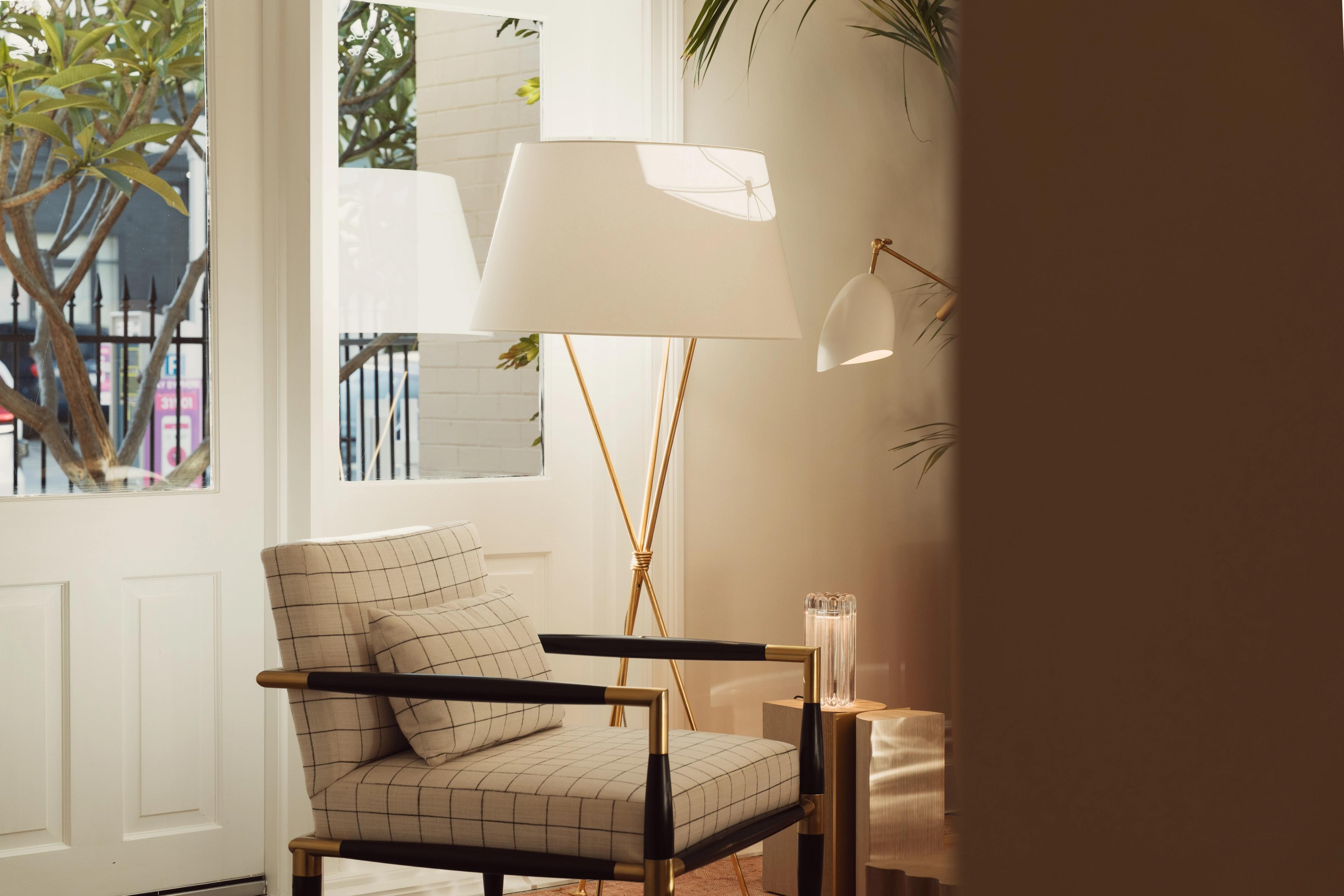 A checked armchair beside a brass tripod floor lamp in morning light