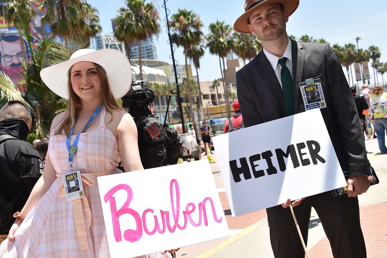 Cosplayers hold Barbenheimer signs outside the convention center during San Diego Comic-Con International