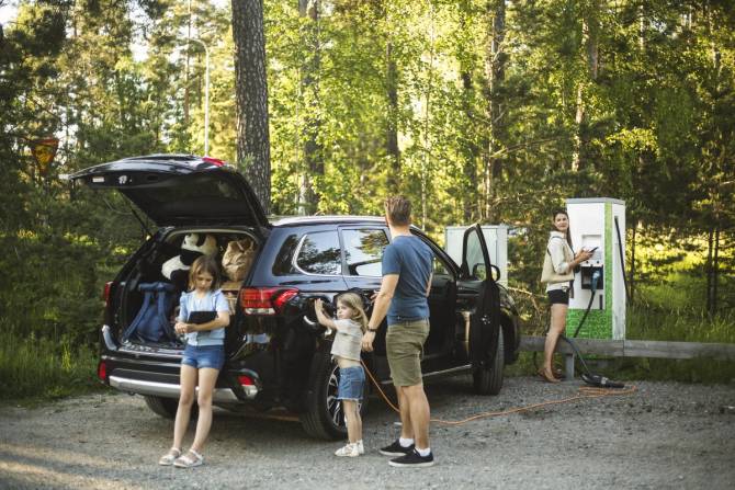 Image of a family hanging out by their car, waiting for it to charge on a road trip.