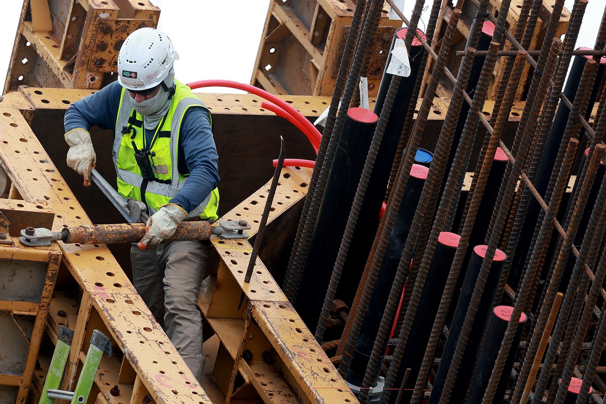 A construction worker using a wrench on a piece of steel.