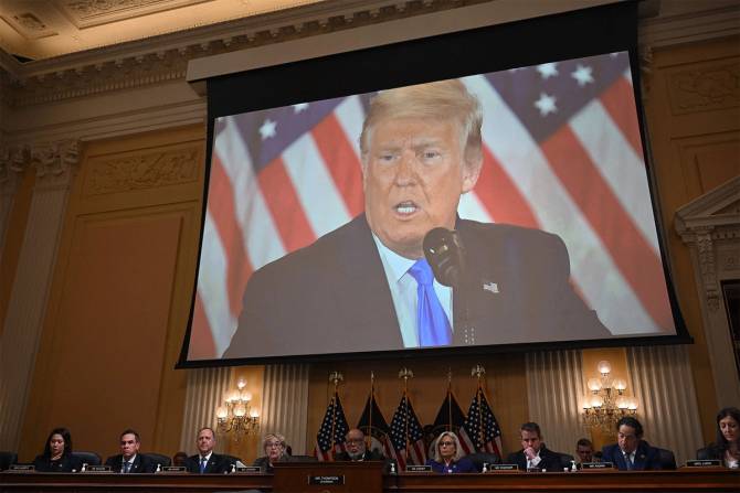 The January 6 Committee beneath a video of former president Donald Trump