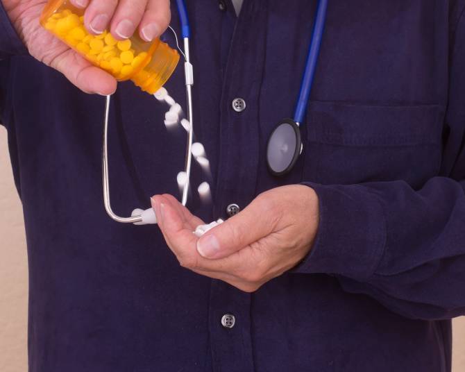 A doctor pours out pills from an orange pill bottle.