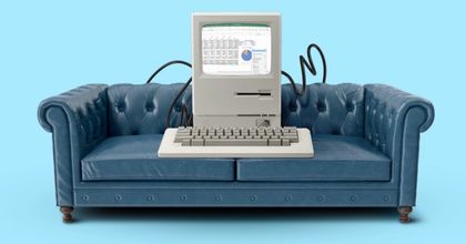 Retro computer with keyboard sitting on a blue and navy couch with wires hanging out of it on a light blue background