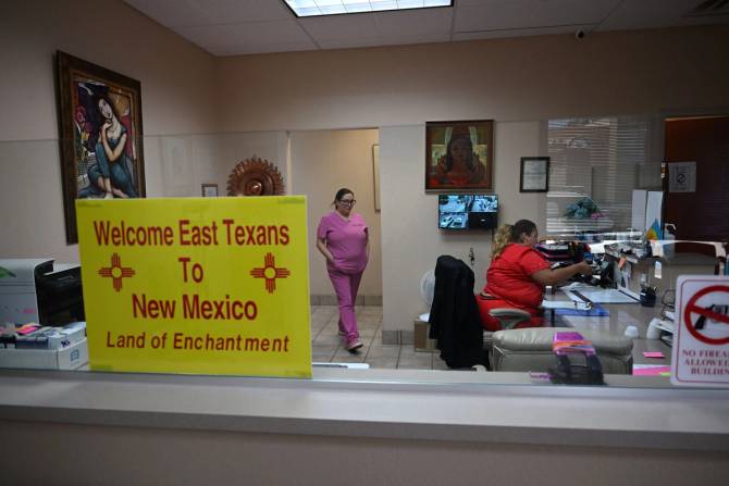 Women working in an office with a sign welcoming East Texans to New Mexico