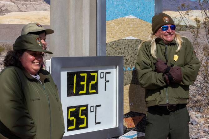 U.S. Park Ranger Eric Henson (R) pretends to be cold while posing next to the unofficial thermometer at the Furnace Creek Visitor Center indicating a temperature of 132 degrees Fahrenheit