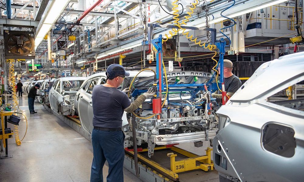 Car workers fitting bonnets to cars on production line in car factory.