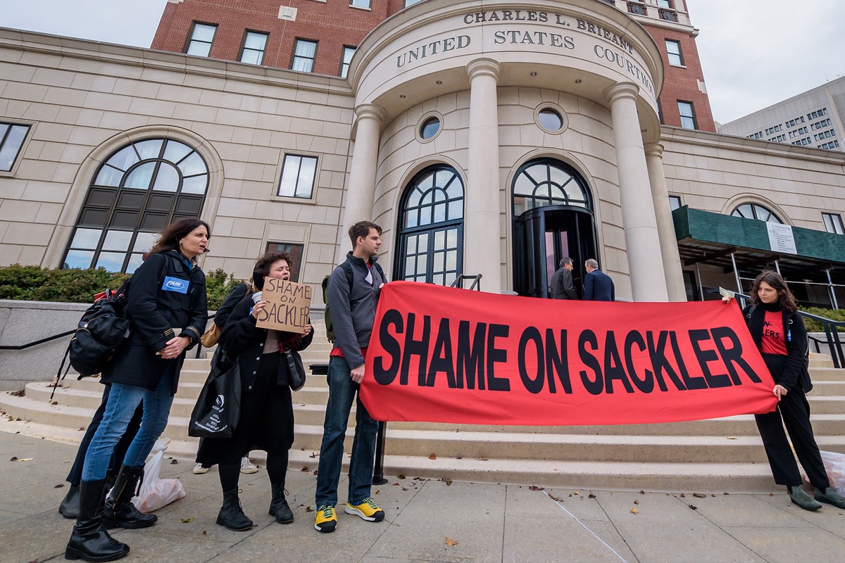 Protesters standing in front of a US courthouse holding a red banner with black text that reads, 'Shame on Sackler'
